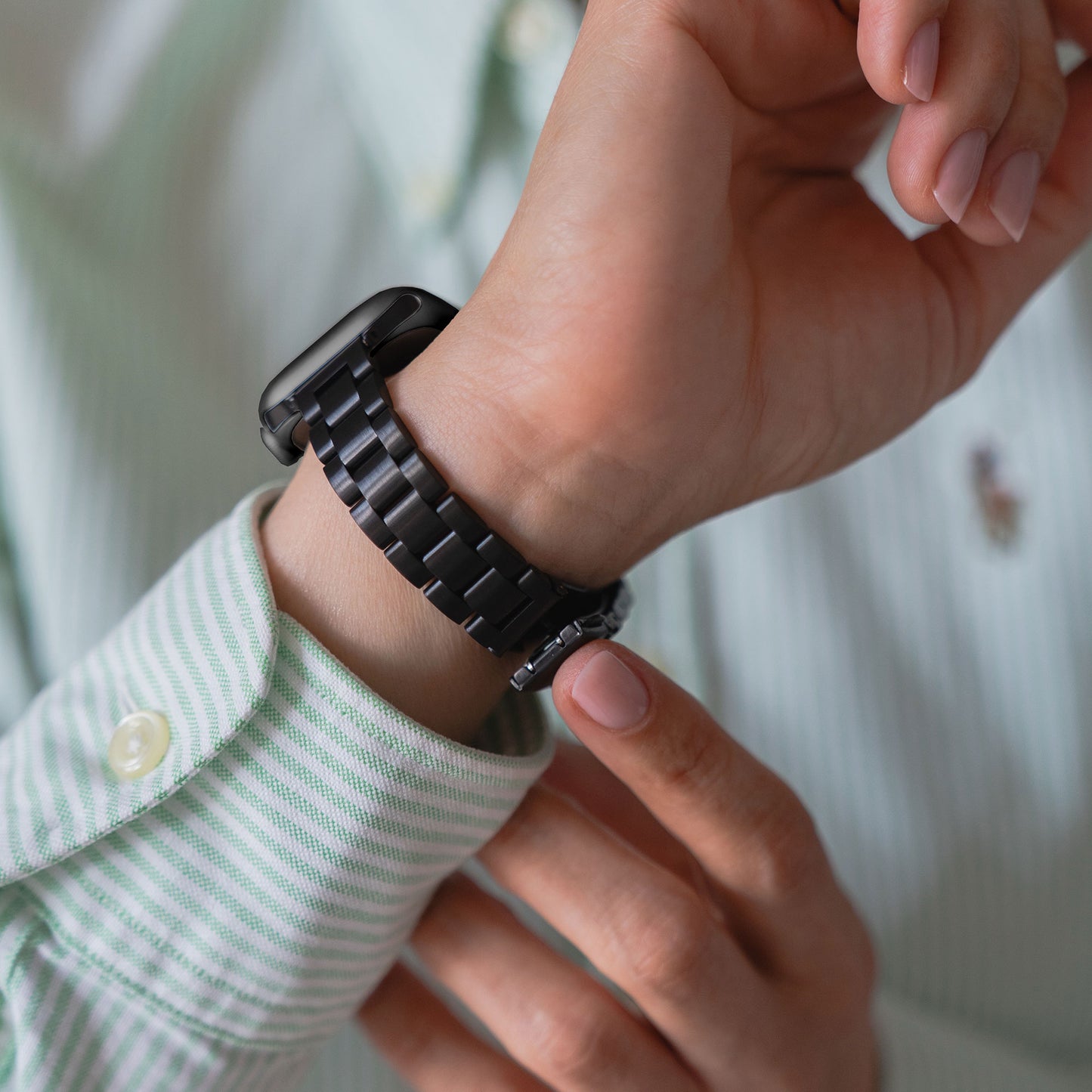 Jemand in einem grün-weiß gestreiften Hemd befestigt das arktisband Apple Watch Gliederarmband „Arctica“ – Slim am linken Handgelenk und präsentiert so elegantes Apple Watch Zubehör von arktisband.
