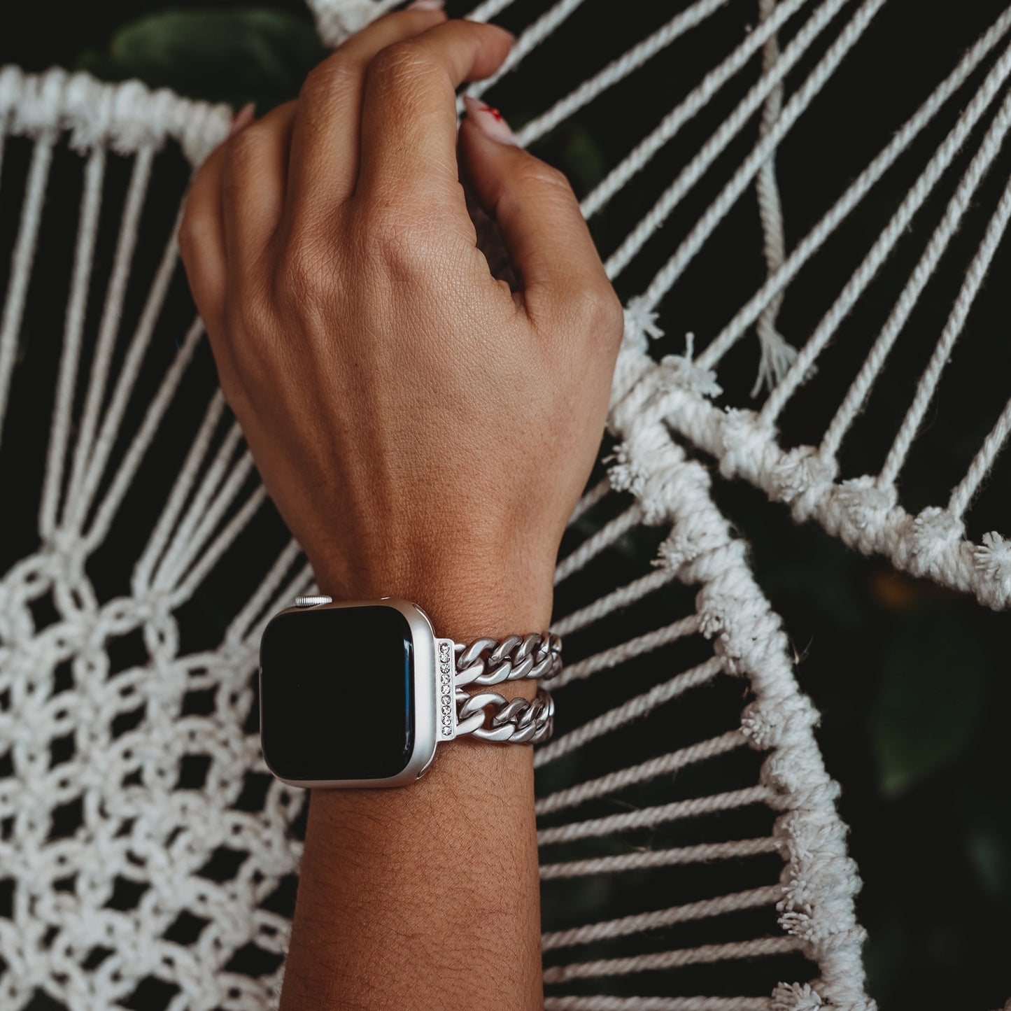 Jemand trägt das arktisband Apple Watch Armband „Princess“ von arktisband mit seinem klobigen silbernen Kettenglied-Design und legt seine Hand auf ein cremefarbenes, geflochtenes Seil. Das Uhrendisplay ist ausgeschaltet, wodurch die glänzende Gliederstruktur des Armbands hervorgehoben wird.