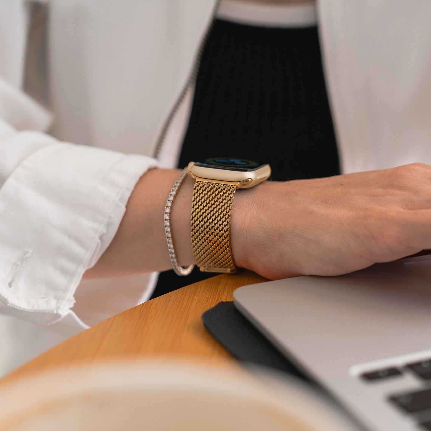Jemand tippt auf einem Laptop und trägt dabei ein Arktisband Apple Watch Milanaise Armband „Bold“ in Gold und ein passendes Armband, beide kompatibel mit der Apple Watch.
