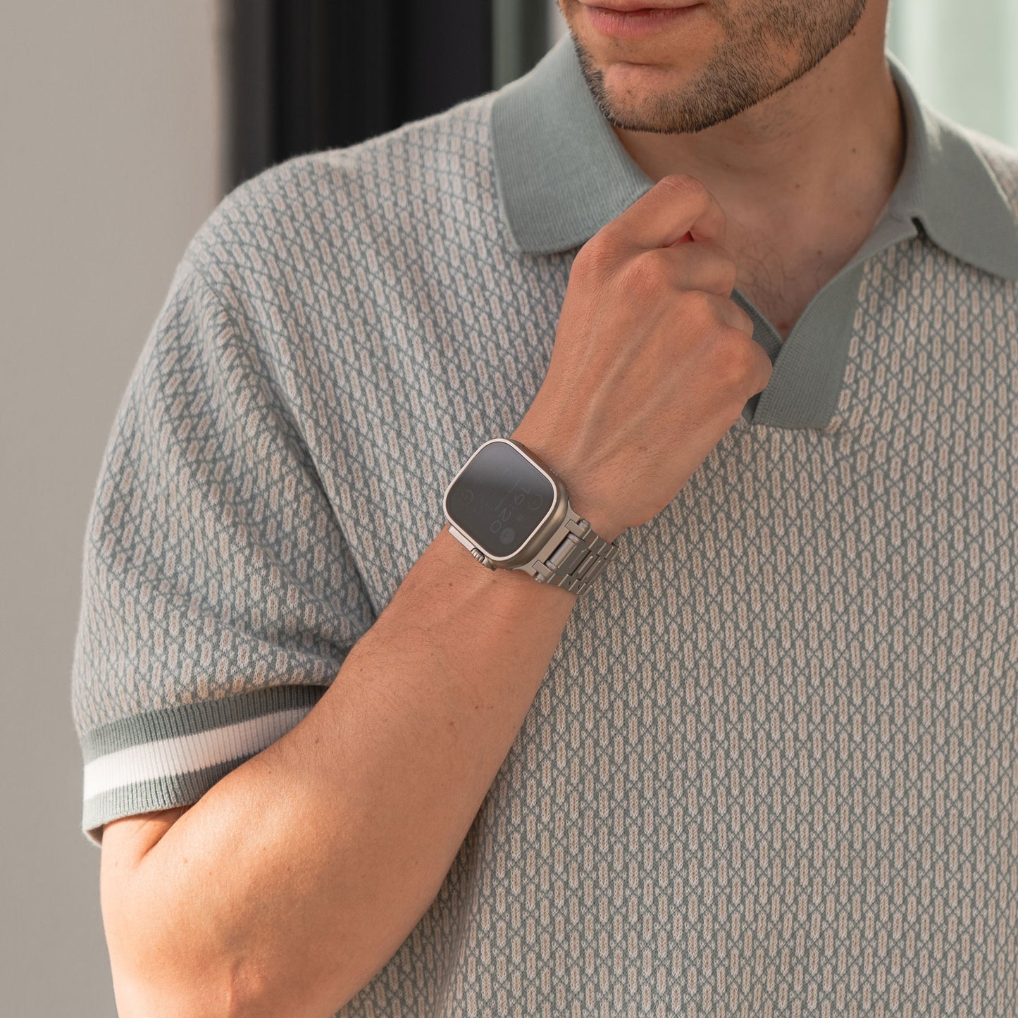 Mann trägt ein gemustertes Poloshirt und eine silberne Smartwatch mit dem Arktisband Apple Watch Armband „TXR-500“ und hält mit einer Hand seinen Kragen.