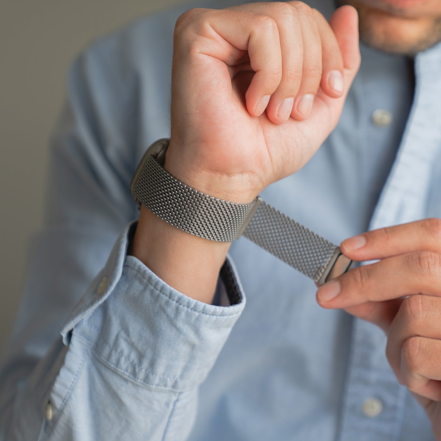 Jemand trägt ein hellblaues Hemd, während er das Arktisband Apple Watch Milanaise Armband "Bold" mit Magnetverschluss an seinem Handgelenk befestigt.