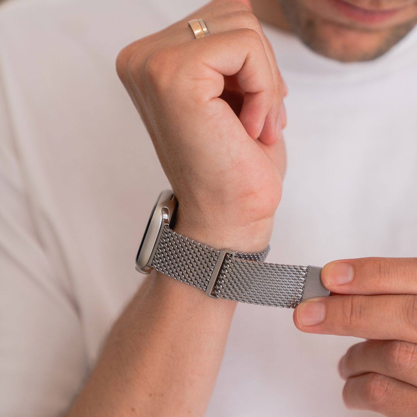 Das arktisband Apple Watch Milanaise Armband "Bold" in Silber wird am Handgelenk befestigt und mit einem weißen Hemd und einem goldenen Ring kombiniert. Das stylische Edelstahl-arktisband ist kompatibel mit der Apple Watch.