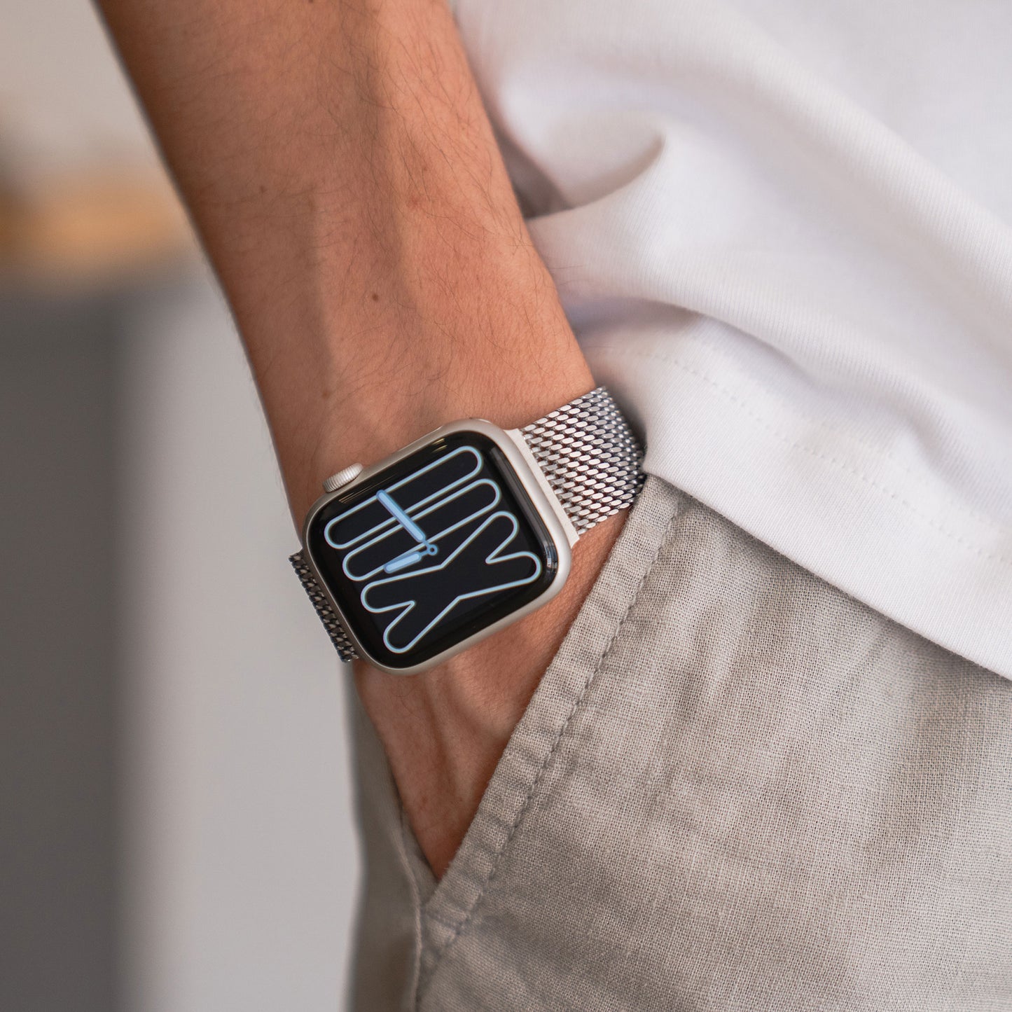 Eine Person trägt das Arktisband Apple Watch Milanaise Armband „Bold“ mit silbernem Mesh-Band, die Hand in der Tasche, bekleidet mit einem weißen Hemd und einer beigen Hose.