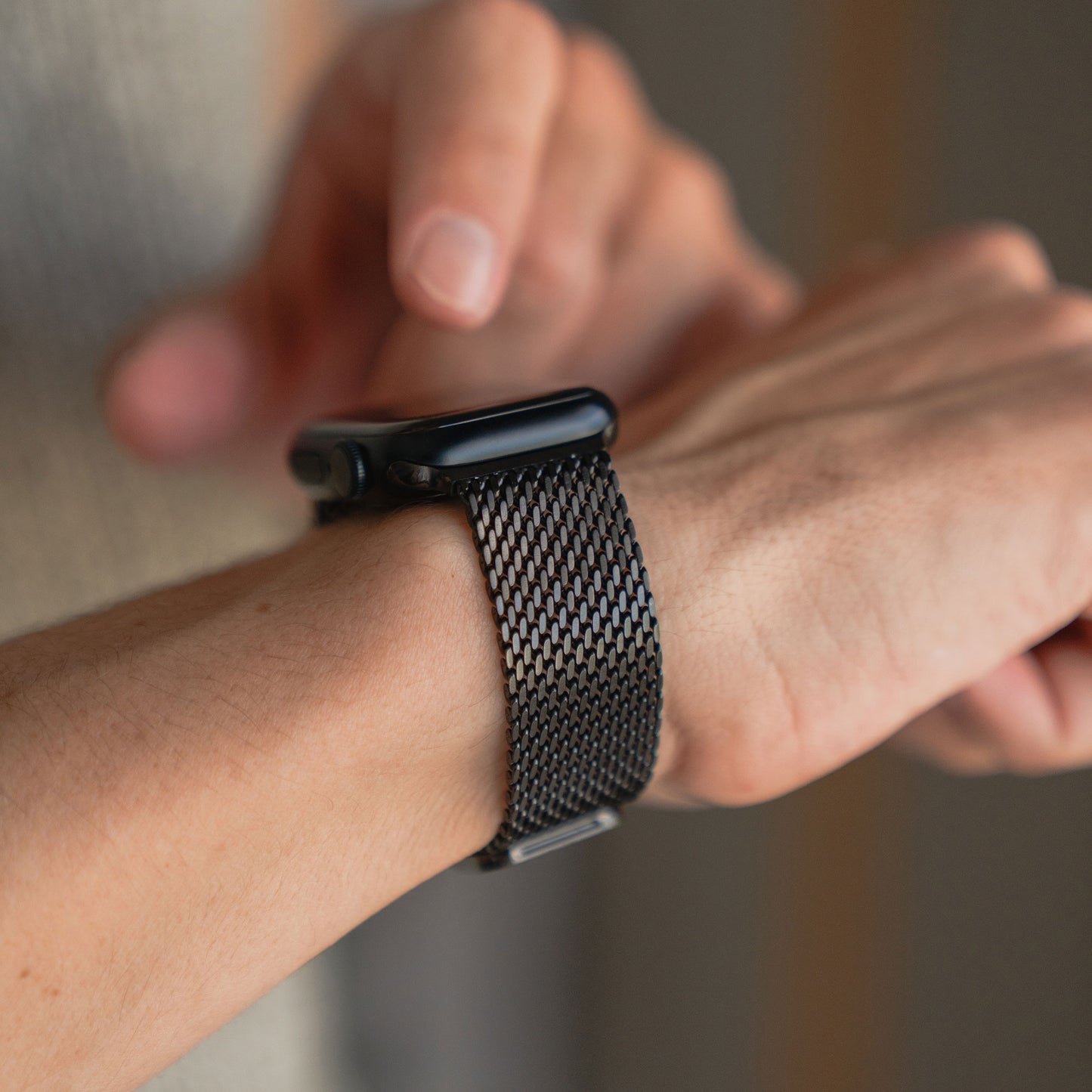 Eine Person passt ihre schwarze Apple Watch mit dem arktisband Apple Watch Milanaise Armband "Bold" von arktisband an ihr Handgelenk an.