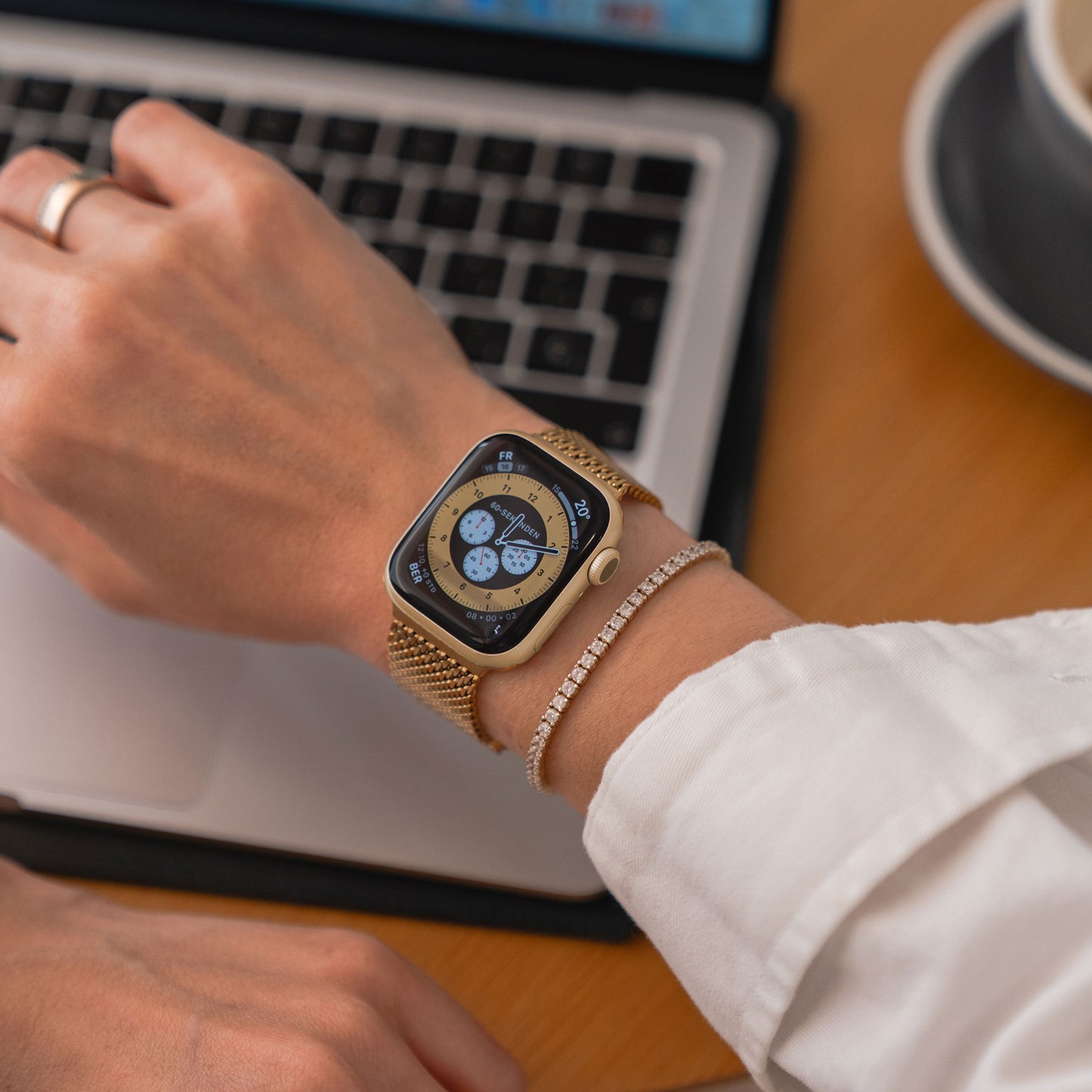 Jemand, der ein Arktisband Apple Watch Milanaise Armband „Bold“ trägt, tippt neben einer Tasse Kaffee auf einem Laptop.