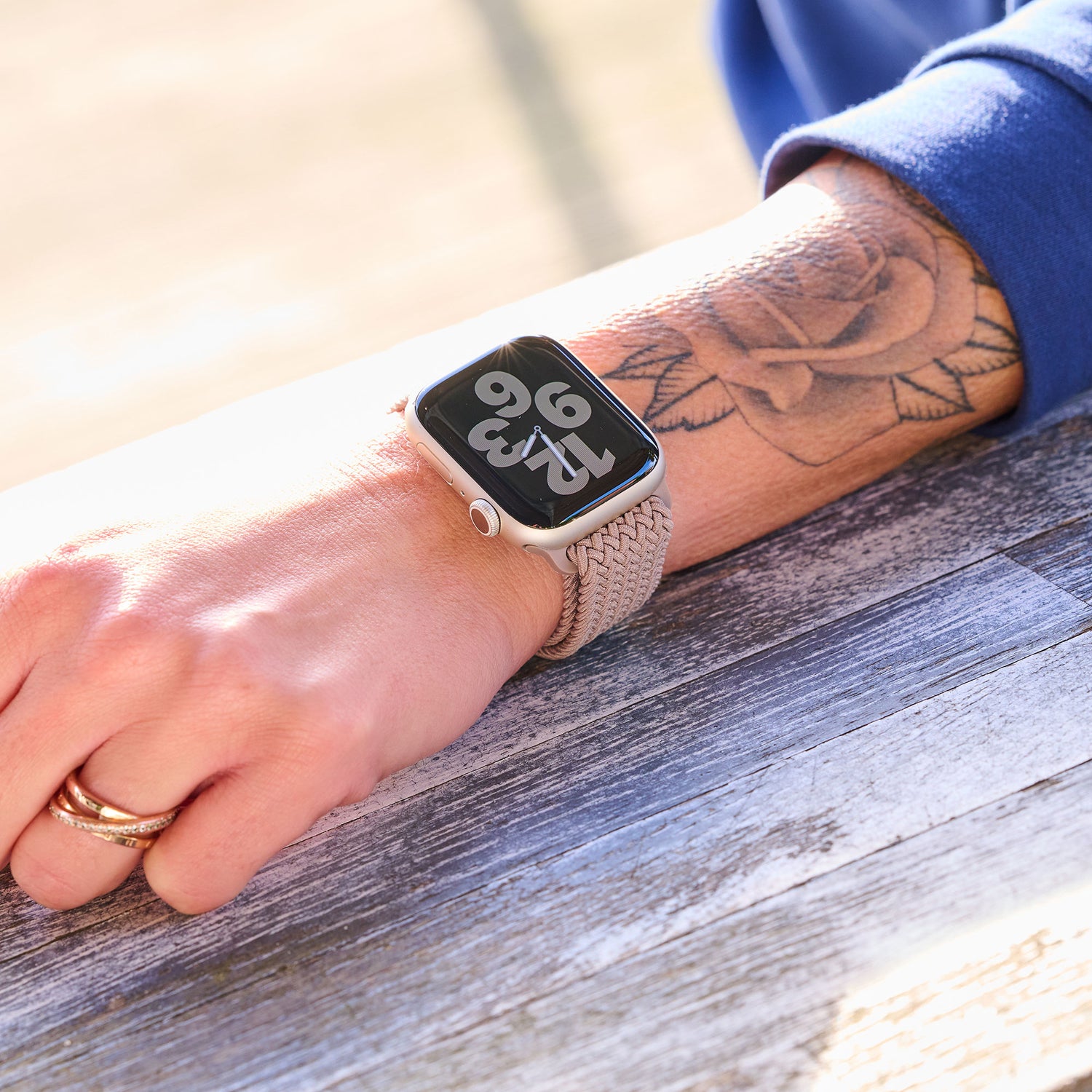 Eine Person mit einem Rosentattoo trägt eine Apple Watch mit großem Digitaldisplay und ein Arktisband Geflochtenes Apple Watch Armband „Casual“ mit Magnetverschluss.