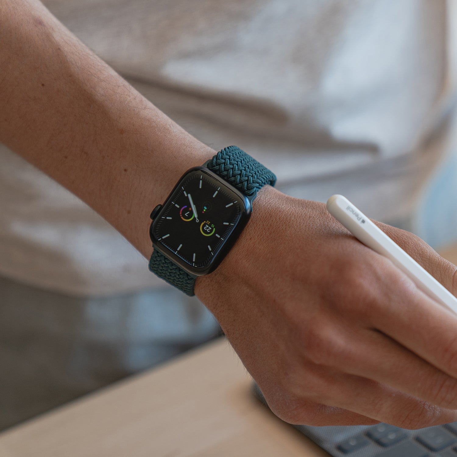 Eine Person, die ein geflochtenes Apple Watch Armband „Casual“ mit Magnetverschluss von Arktisband trägt, schreibt mit einem weißen Stift an einem Schreibtisch.
