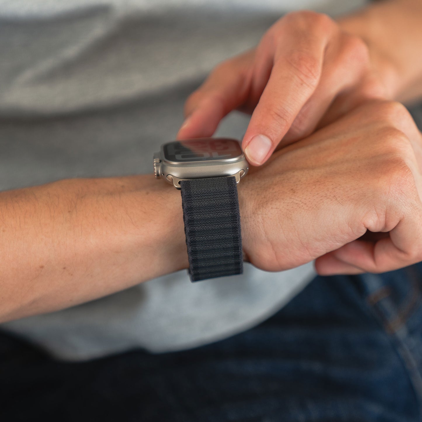 Eine Person, die ein schwarzes Arktisband-Nylonarmband „Venture“ für die Apple Watch trägt, berührt mit der anderen Hand den Bildschirm ihrer Smartwatch und ist bereit für Abenteuer.