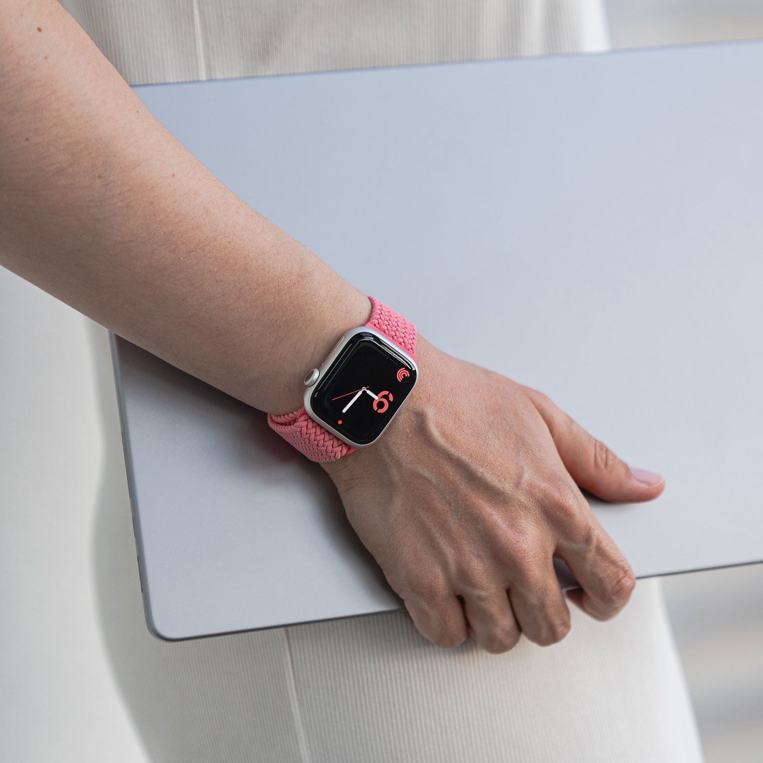 Eine Person hält einen geschlossenen Laptop und trägt ein arktisband Geflochtenes Apple Watch Armband „Casual“ mit Magnetverschluss in Pink am Handgelenk.