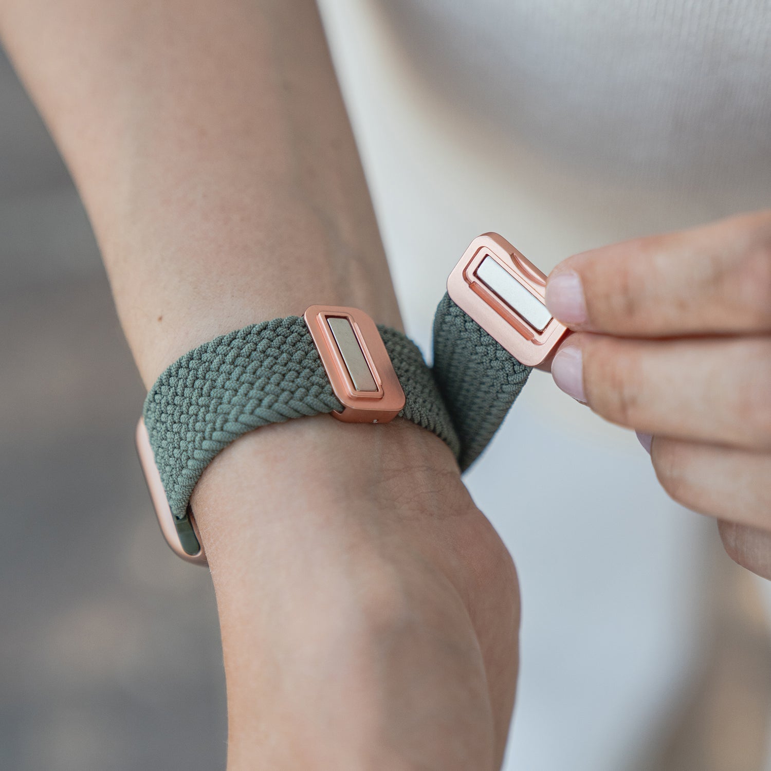 Eine Person befestigt das arktisband Geflochtene Apple Watch Armband „Casual“ mit Magnetverschluss von arktisband mit grünem Flechtdesign und roségoldenem Magnetverschluss am Handgelenk.