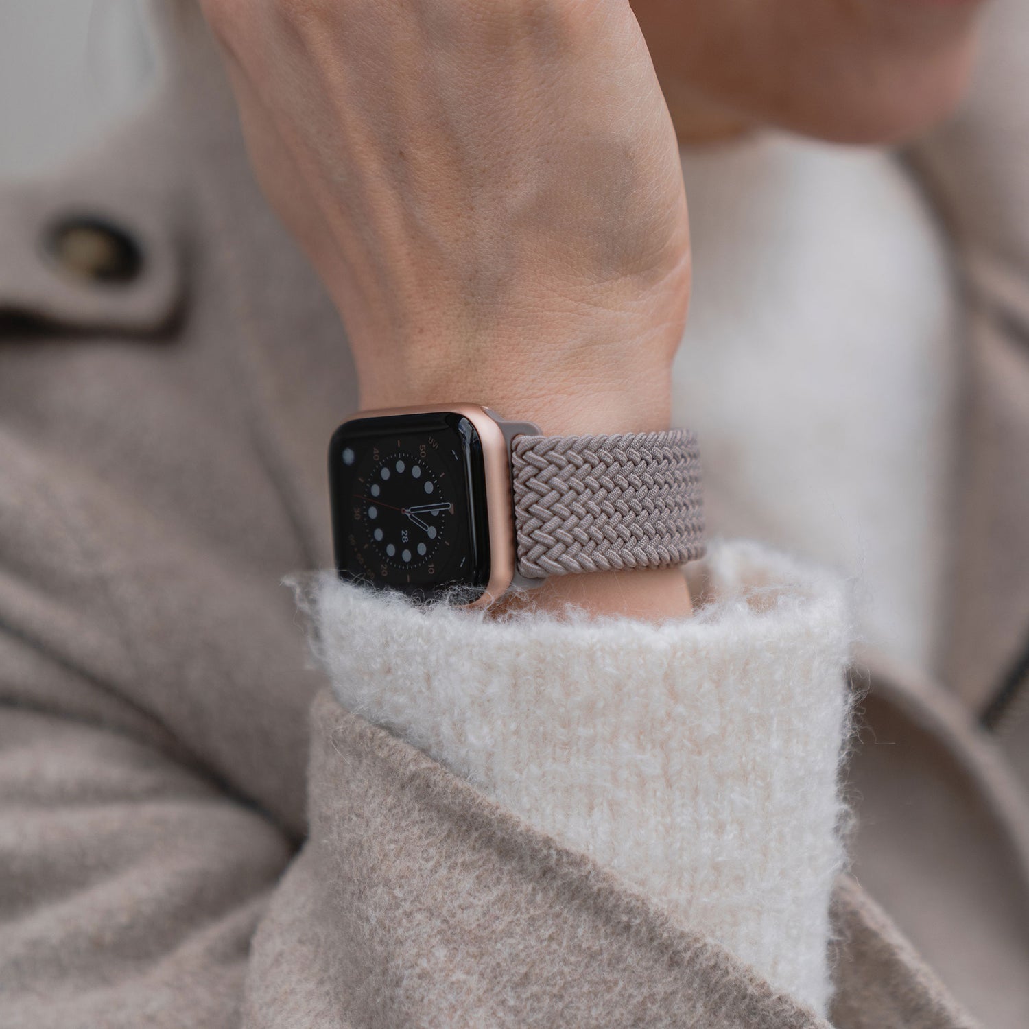 Eine Person trägt ein geflochtenes Apple Watch Armband „Casual“ mit Magnetverschluss von arktisband, kombiniert mit einem beigen Mantel, die Hand vor dem Gesicht.
