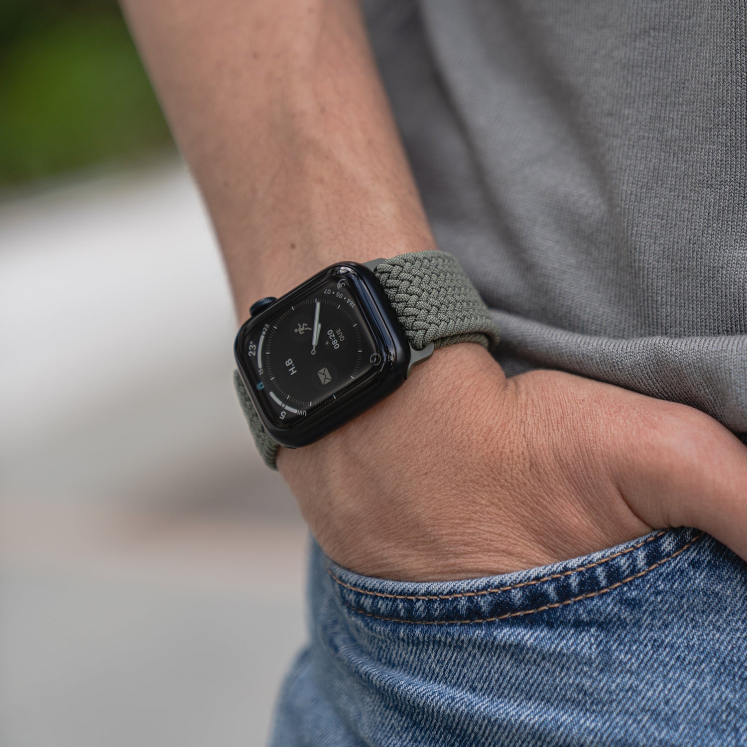 Eine Person trägt das kunstvoll geflochtene Apple Watch Armband „Casual“ mit Magnetverschluss in Grün, hat die Hand in der Tasche und ist mit Jeans sowie grauem Shirt gekleidet.