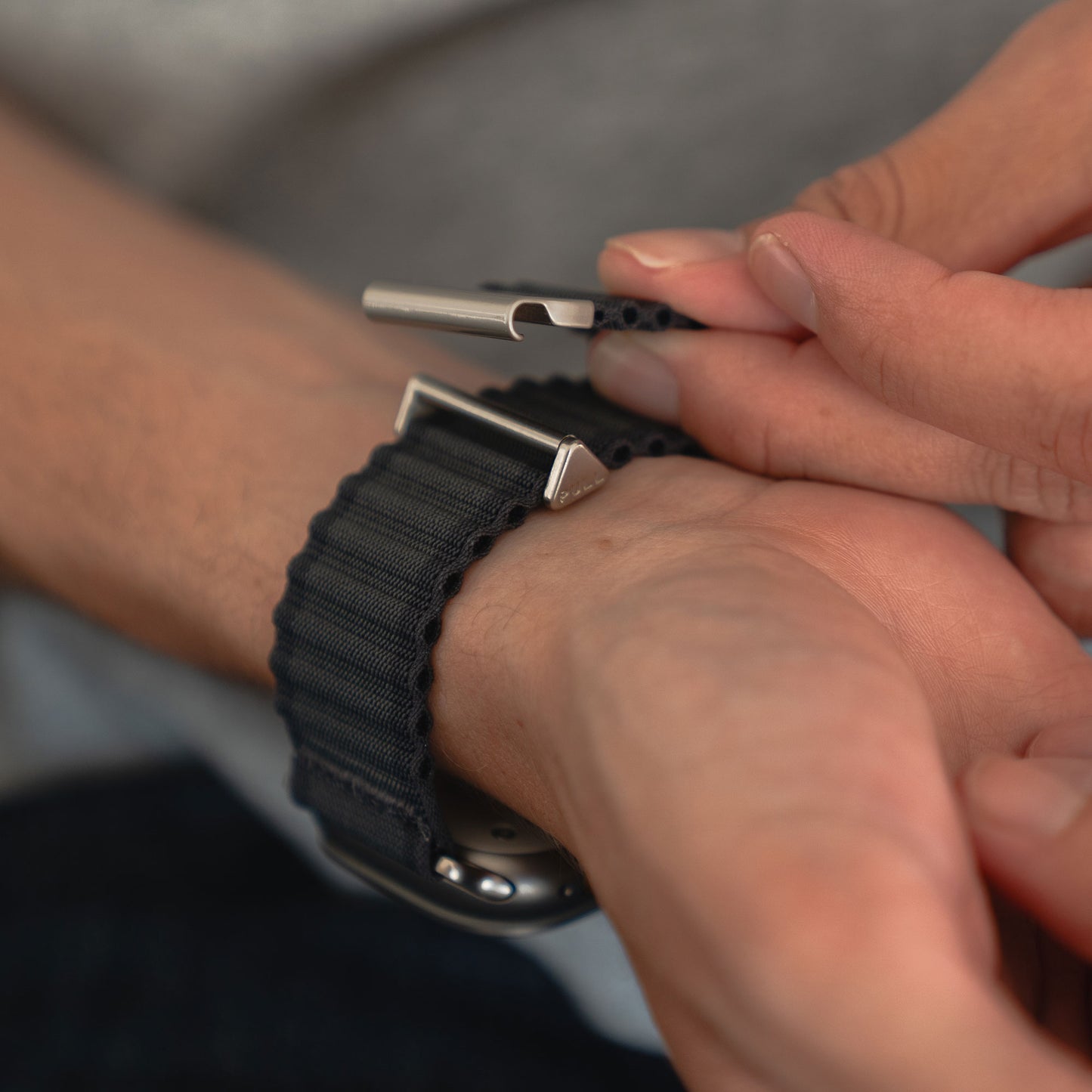 Nahaufnahme von Händen, die ein Arktisband Apple Watch Nylonarmband „Venture“ an einem Handgelenk befestigen, perfekt für jedes Abenteuer und mit elegantem Wellen-Look.