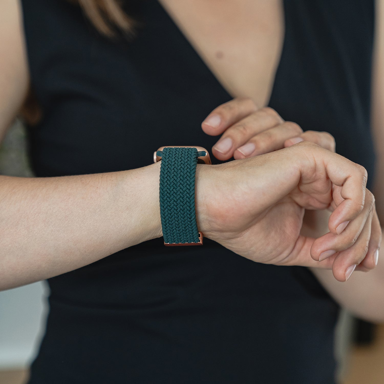 Eine Person in einem ärmellosen schwarzen Top passt ihr arktisband Geflochtenes Apple Watch Armband „Casual“ mit Magnetverschluss in Dunkelgrün an.