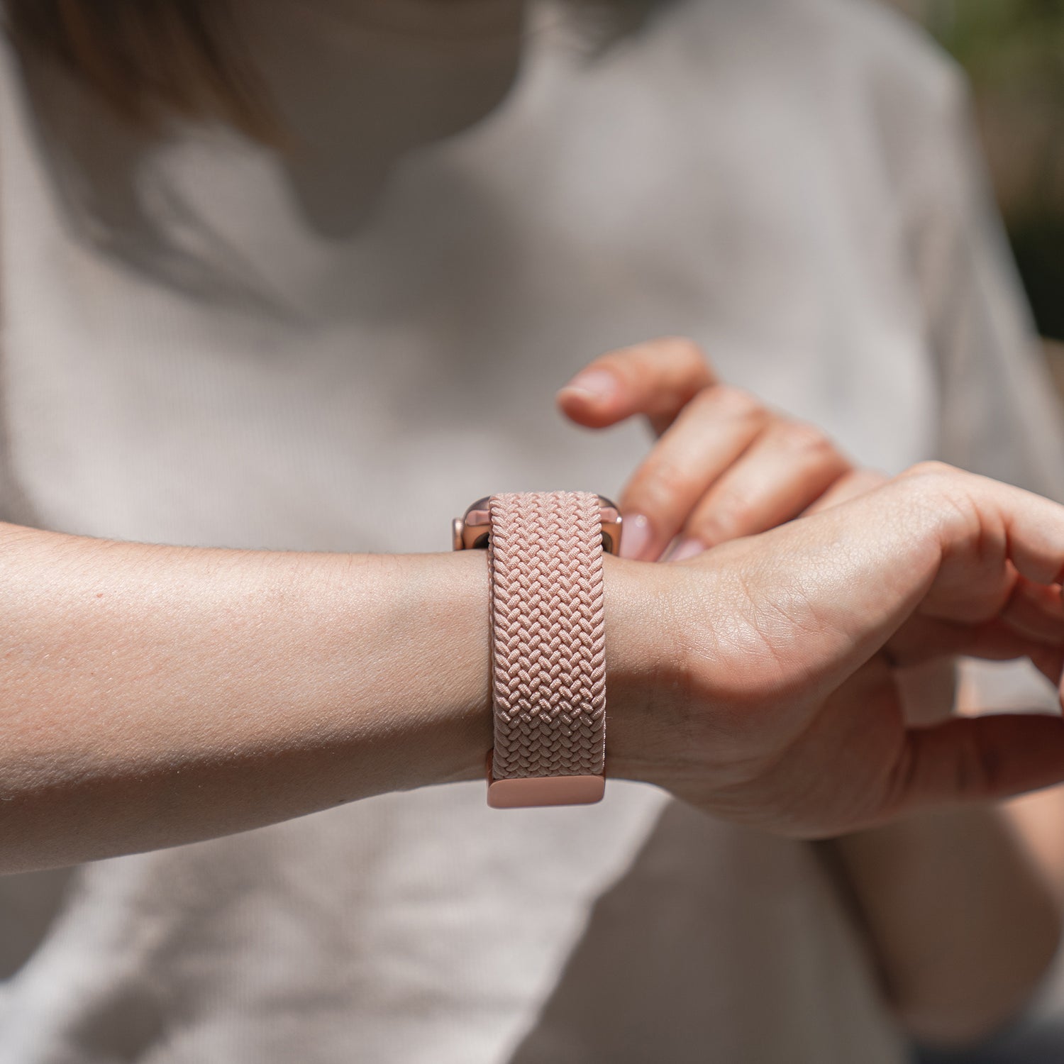 Jemand mit einem hellen Hemd berührt sein Handgelenk, an dem sich ein arktisband Geflochtenes Apple Watch Armband „Casual“ mit Magnetverschluss von arktisband in Pink an seiner Apple Watch befindet.