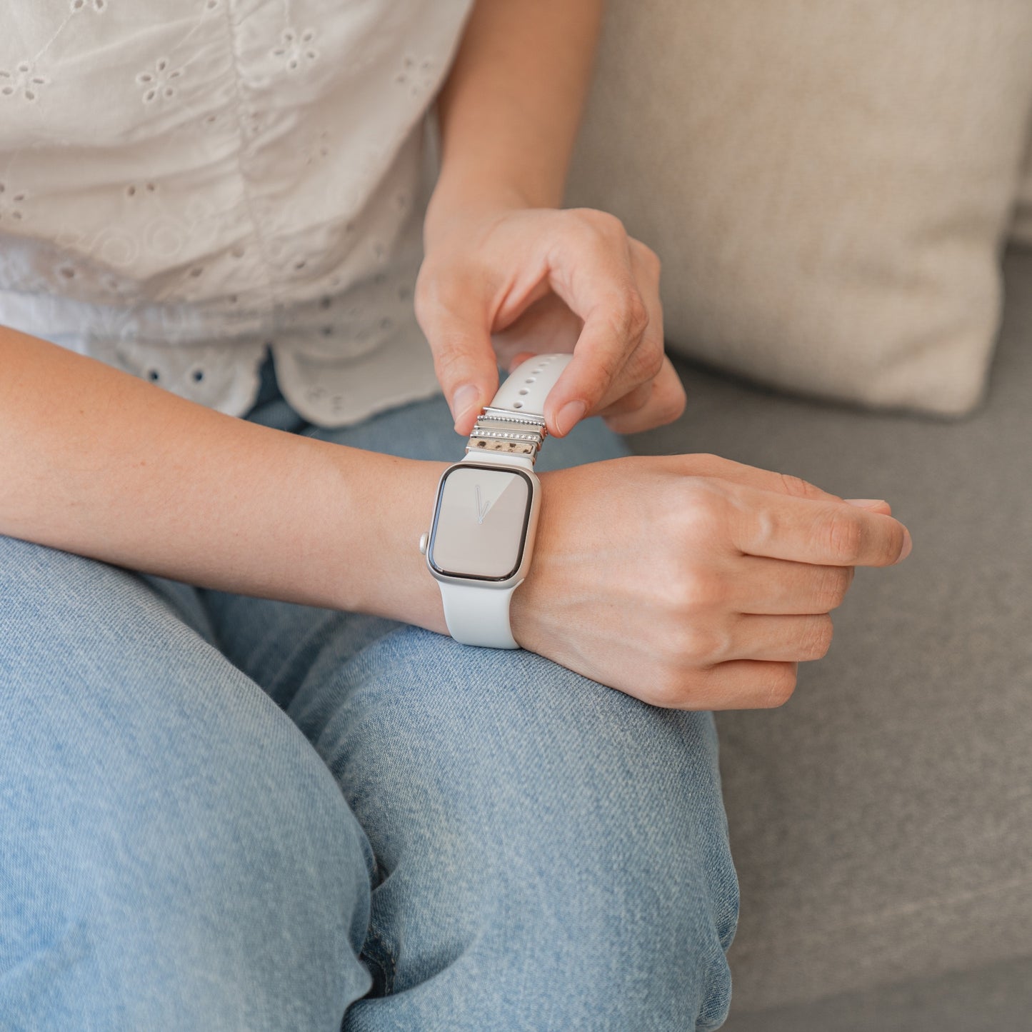 Person, die in Jeans auf einem Sofa sitzt und auf ihrer Apple Watch mit einem silbernen Anhänger „Leopard Style“ von Arktisband die Uhrzeit überprüft.