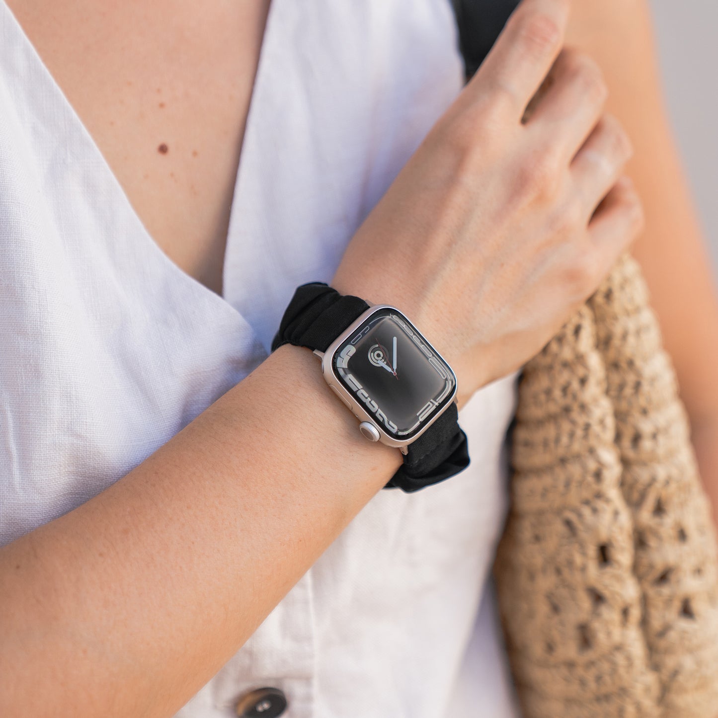 Person trägt ein arktisband Apple Watch Scrunchie Armband "Elanora" von arktisband, gepaart mit einer gewebten Tasche und einem weißen ärmellosen Oberteil.