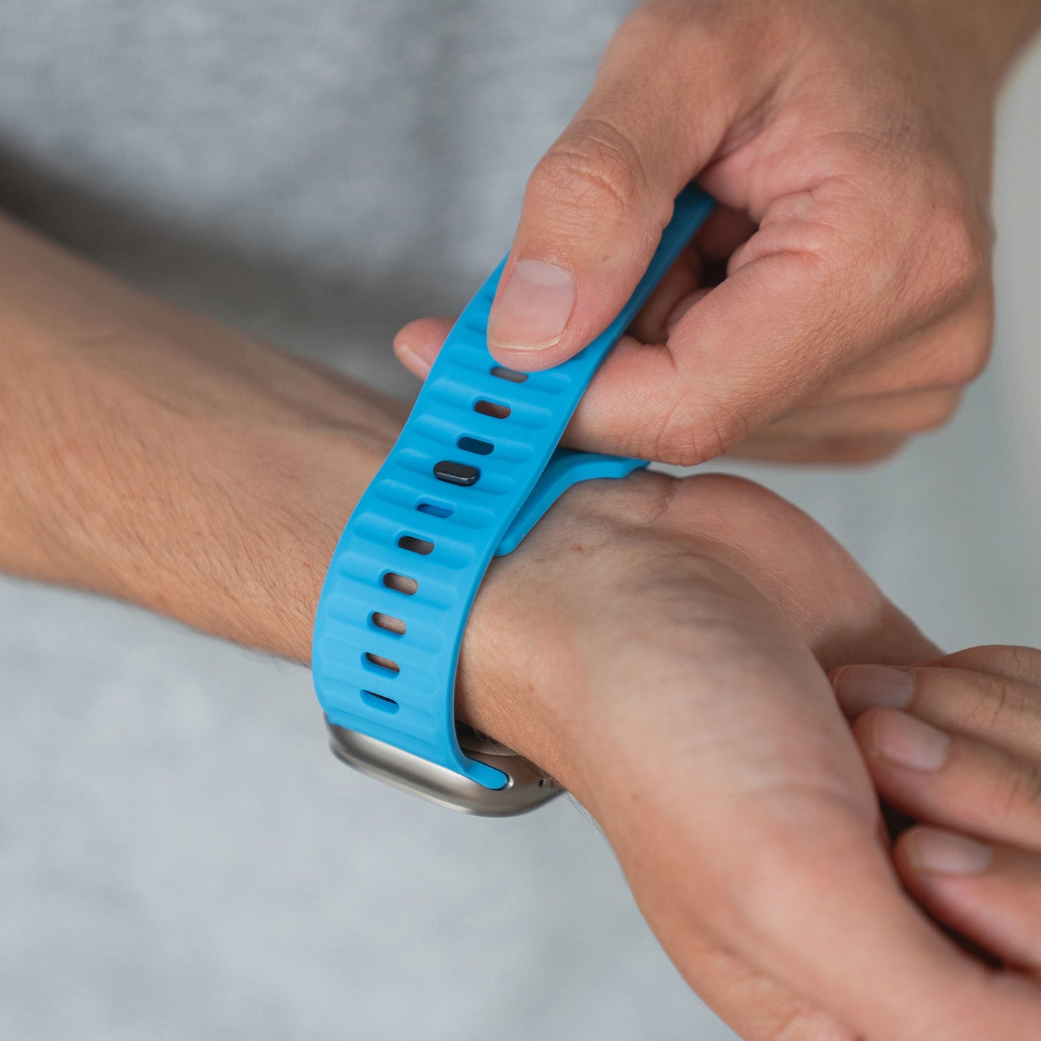 Eine Person befestigt das arktisband Apple Watch Silikonarmband „Active“ von arktisband an ihrem Handgelenk und präsentiert sein atmungsaktives und bequemes Design vor einem schlichten Hintergrund.