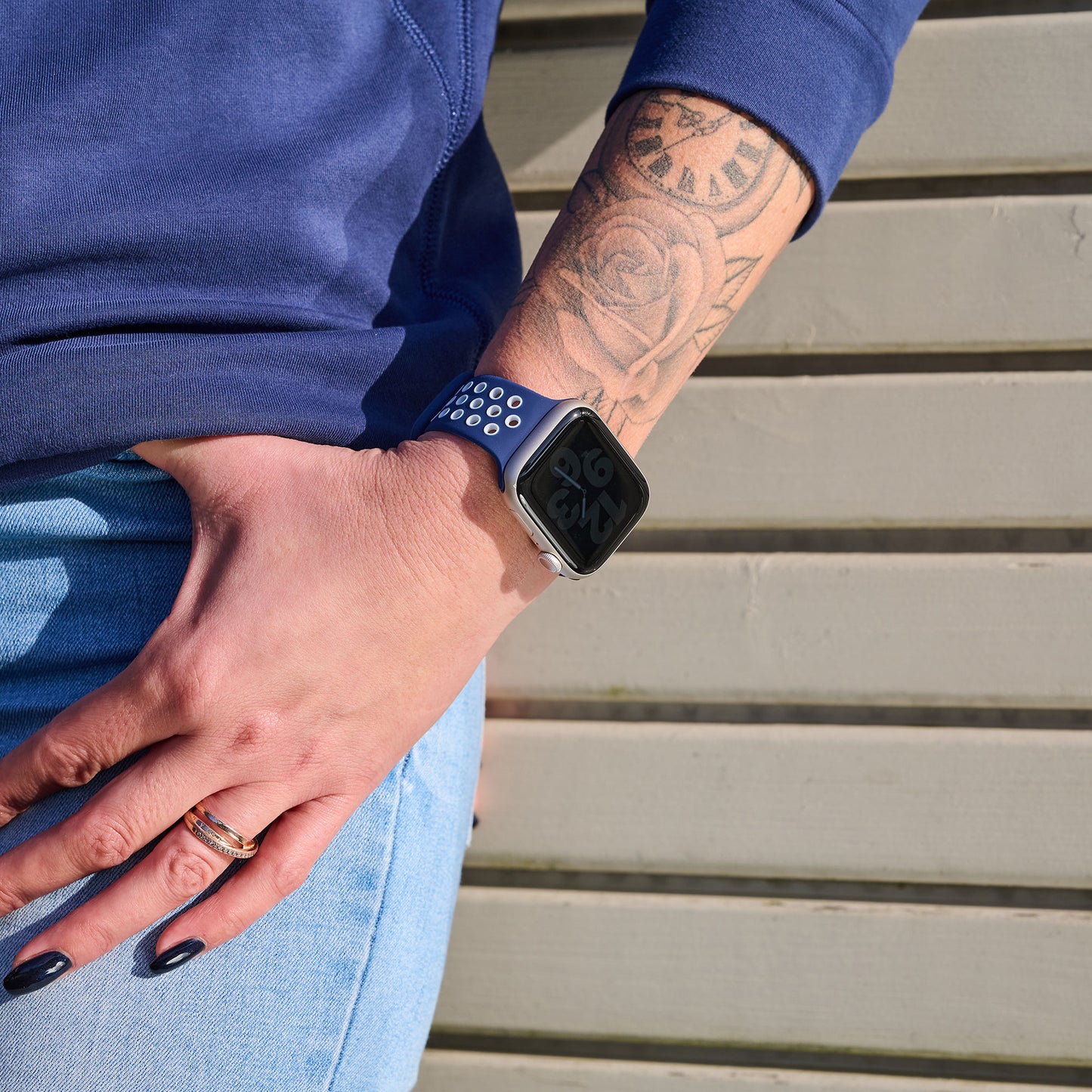 Jemand trägt ein Arktisband Apple Watch Silikonarmband „Energy“ in Blau und hat die Hand in der Tasche. Auf dem Unterarm ist ein Uhrentattoo zu sehen, er trägt Blue Jeans und ein marineblaues Oberteil und trägt einen goldenen Ring.