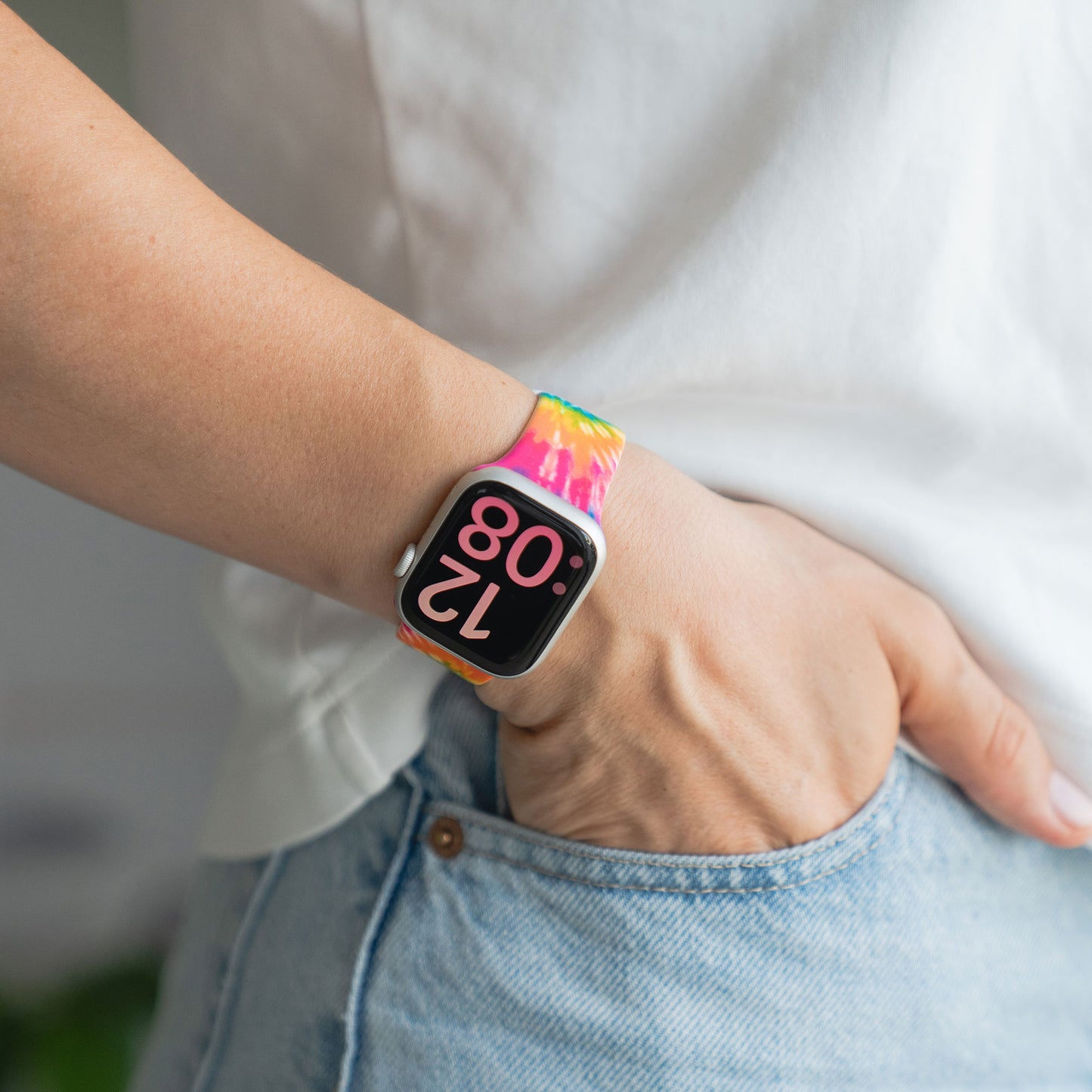 Eine Person trägt eine arktisband EDITION für Apple Watch mit einem bunten Silikonarmband von arktisband und digitaler Zeitanzeige, Hand in blauer Jeanstasche.