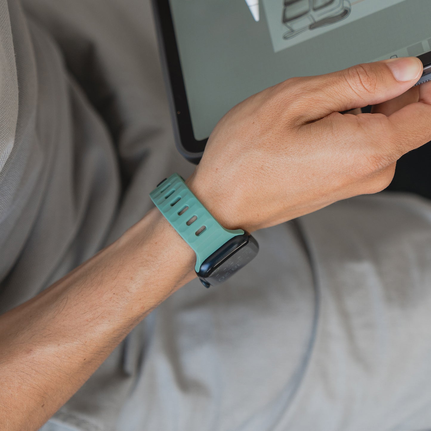 Eine Person trägt ein grünes Arktisband Apple Watch Silikonarmband „Active“ und hält einen Stift, während sie ein Tablet benutzt. Die Person ist hell gekleidet und sitzt bequem.