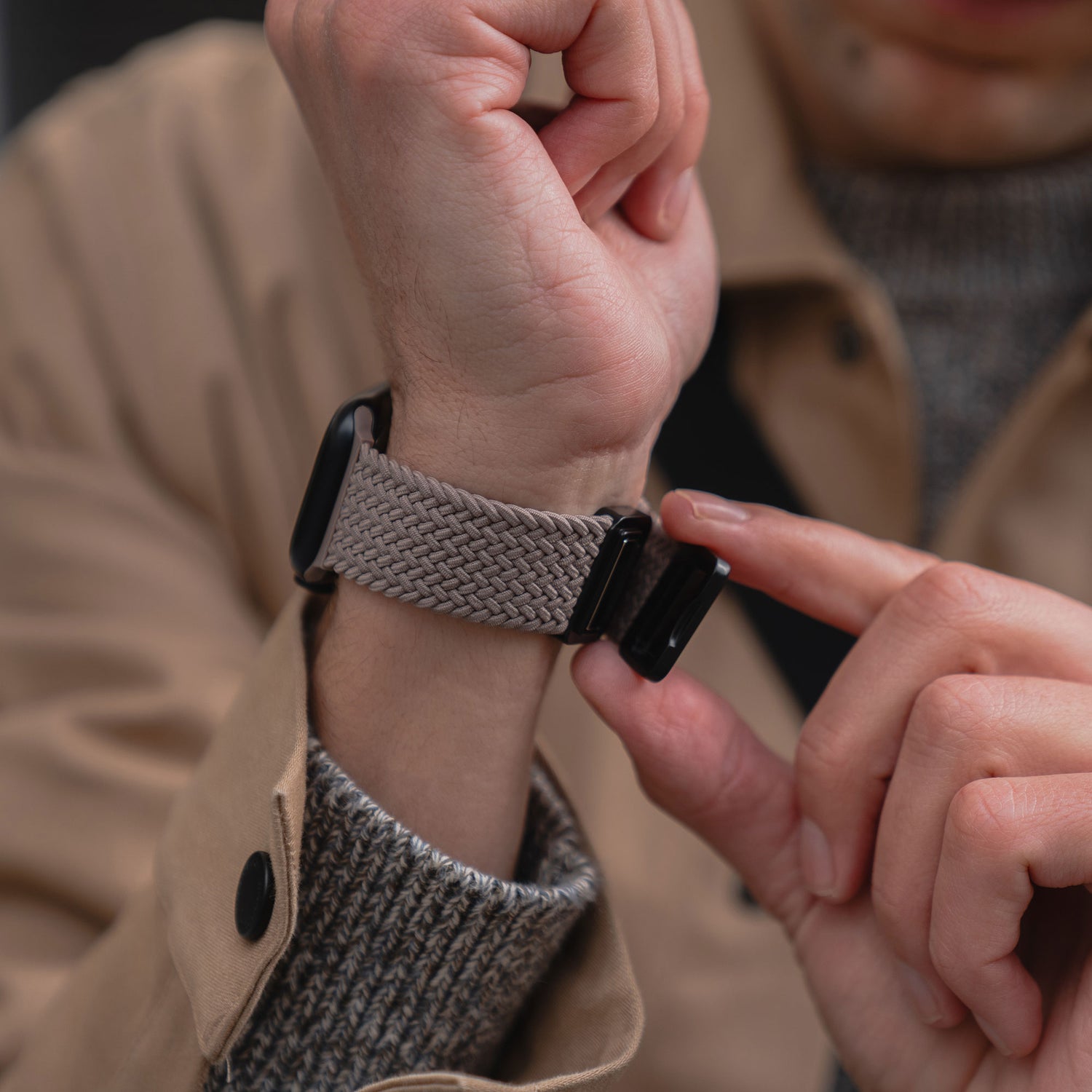 Jemand stylt seine Apple Watch mit dem arktisband Geflochtenen Apple Watch Armband "Casual" mit Magnetverschluss, beige, kombiniert mit einem hellbraunen Mantel und einem grauen Pullover.