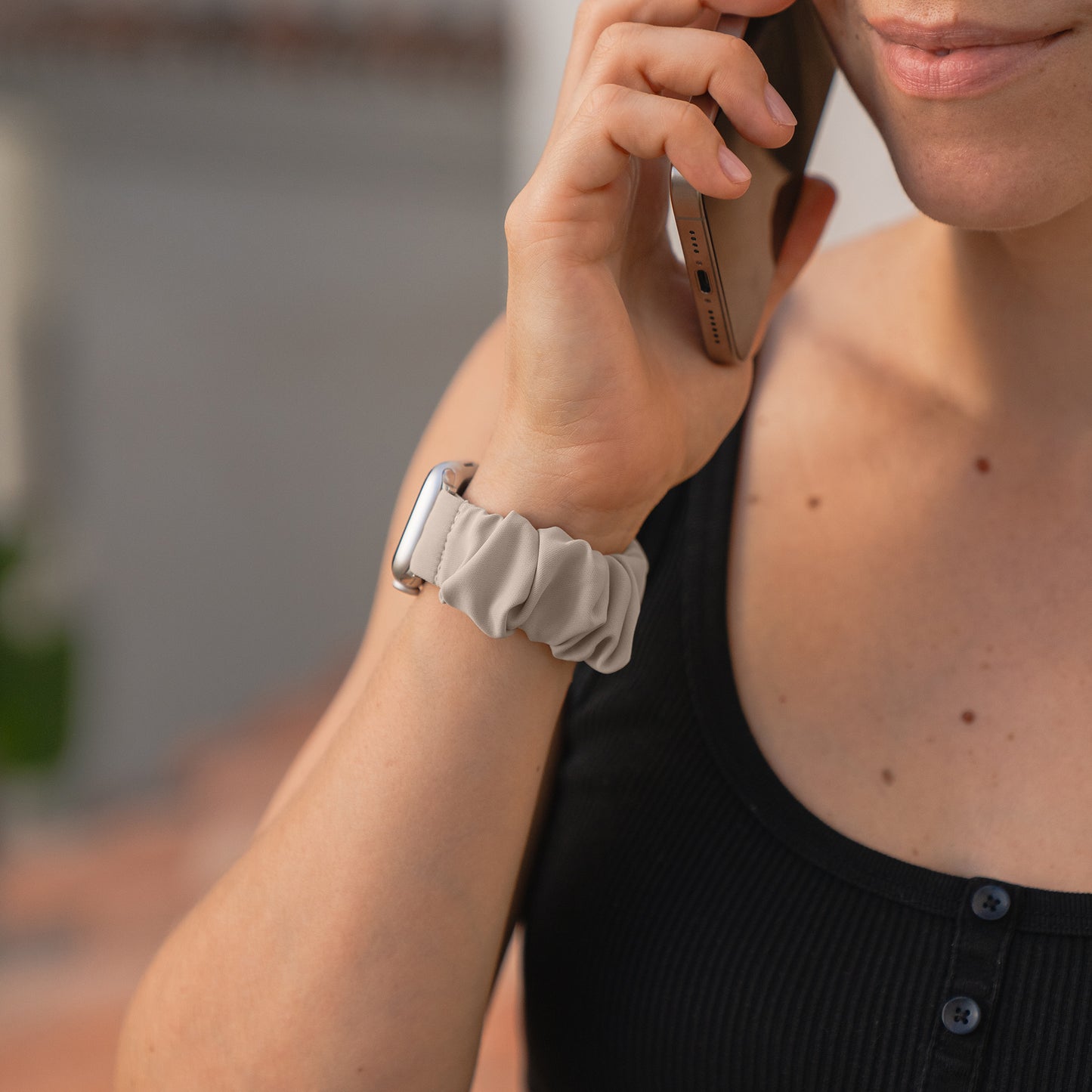 Eine Person in einem schwarzen Tank-Top telefoniert, sie trägt ein arktisband Apple Watch Scrunchie Armband "Elanora", ein helles, elastisches Armband von arktisband.