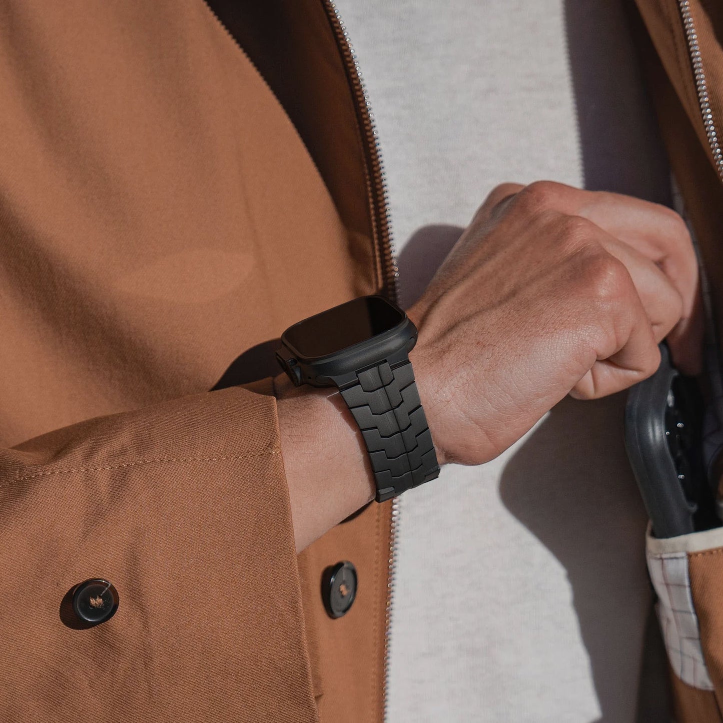 Eine Person in einer braunen Jacke und einem weißen Hemd rückt das arktisband Apple Watch Ultra Armband TITANIUM F-15 von arktisband an ihrem Handgelenk zurecht, während sie in der anderen Hand eine Sonnenbrille hält.