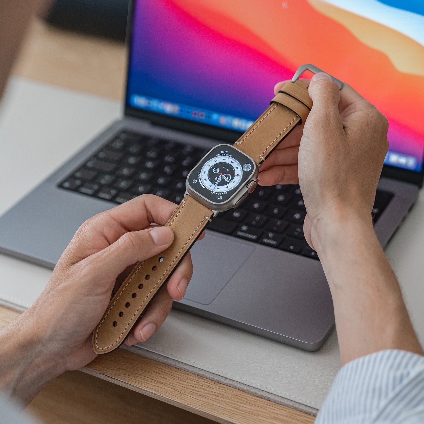 Jemand hält eine Apple Watch Ultra mit dem arktisband PALERMO GRANDE Lederarmband vor einen offenen Laptop mit buntem Display.