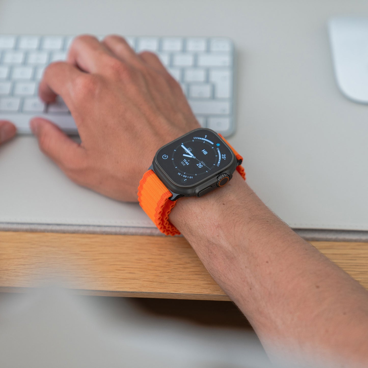 Eine Person mit dem arktisband Apple Watch Nylonarmband „Venture“ bedient eine weiße Tastatur auf einem hellen Schreibtisch. Die arktisband Smartwatch zeigt Uhrzeit und wichtige Messwerte an – ideal für Outdoor-Fans.