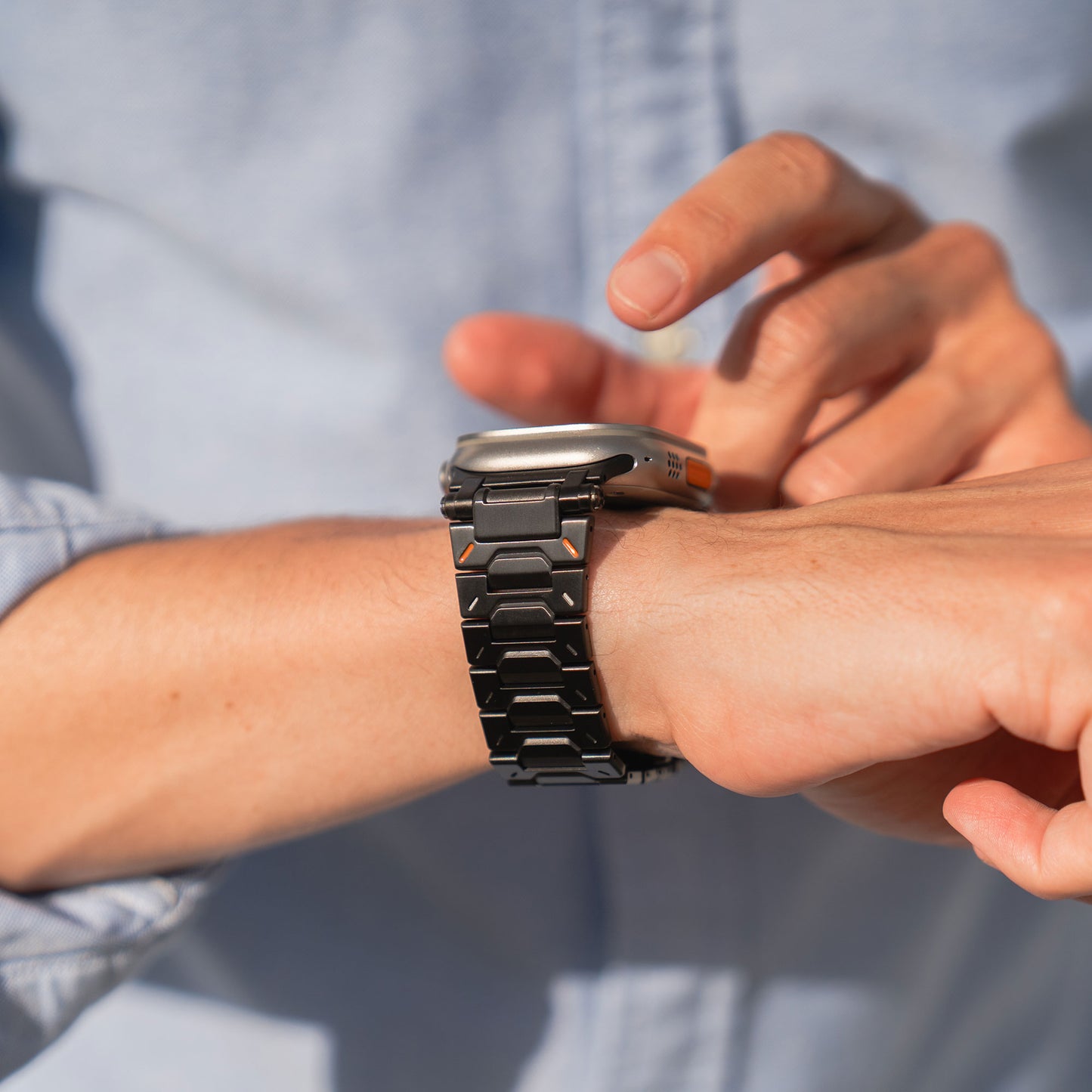 Eine Person trägt das arktisband Apple Watch Armband „TXR-500“ mit einem eleganten 316 Edelstahlband und Butterfly-Schließe und passt es an ihrem Handgelenk an, während sie ein hellblaues Hemd trägt.