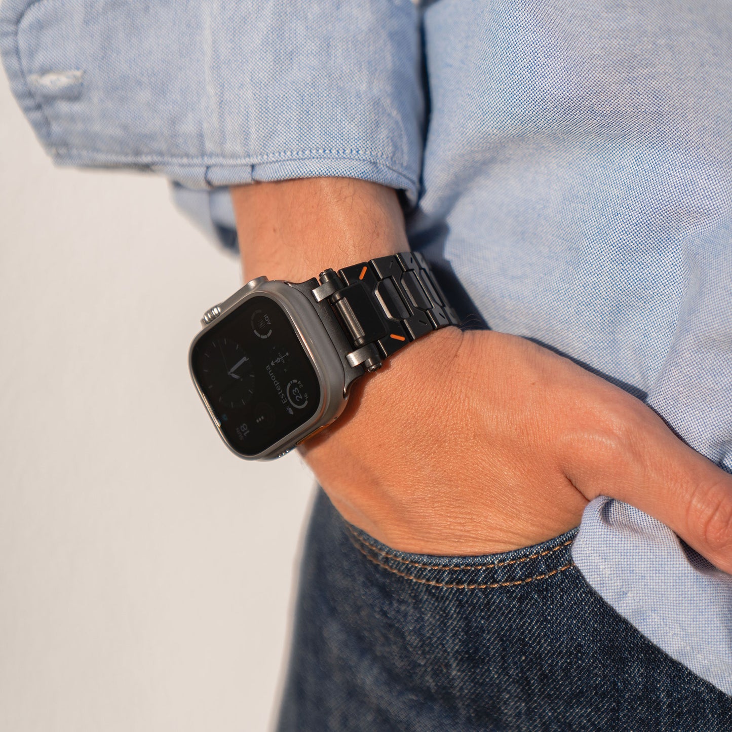 Eine Person trägt ein arktisband Apple Watch Armband „TXR-500“ mit silbernem Gehäuse, schwarzem Armband und glattem Butterfly-Verschluss. Ihre linke Hand steckt in der Hosentasche einer Blue Jeans. Sie trägt ein hellblaues Langarmshirt. Das Uhrendisplay ist teilweise sichtbar.
