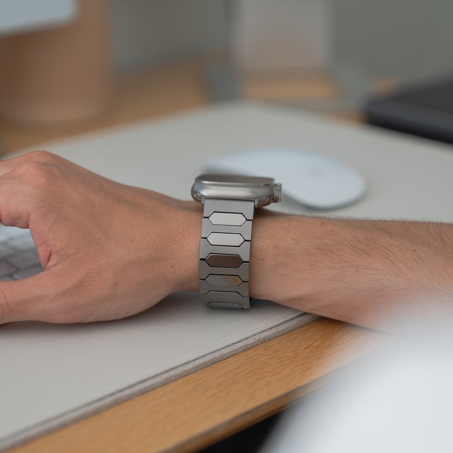 Eine Person, die das arktisband Apple Watch Ultra Titanarmband "Vectoron" von arktisband im modernen, hypoallergenen Design mit DLC-Beschichtung trägt, tippt auf einer Tastatur am Schreibtisch.
