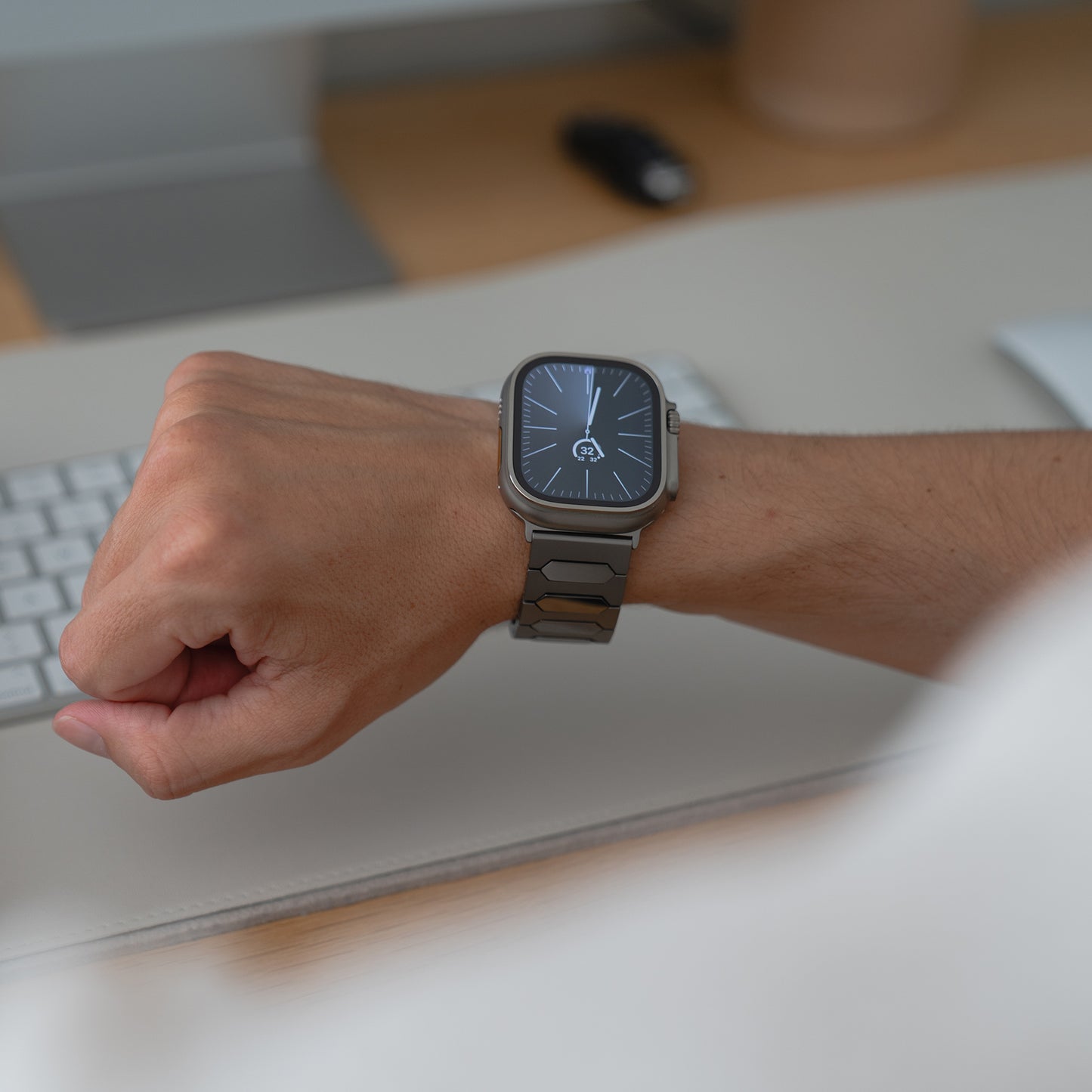 Jemand, der eine arktisband Apple Watch Ultra Titanarmband "Vectoron" mit einem silbernen Band trägt, sitzt an einem Schreibtisch mit einer Tastatur.