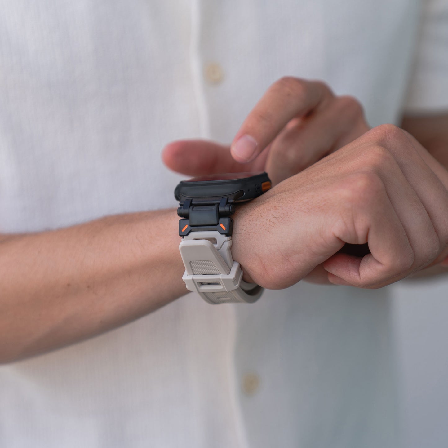 Eine Person in einem weißen Hemd berührt den Bildschirm einer Apple Watch Ultra mit einem Arktisband „Atlas“ von Arktisband, mit Edelstahl-Elementen und einem robusten grau/weißen Band mit orangefarbenen Akzenten.