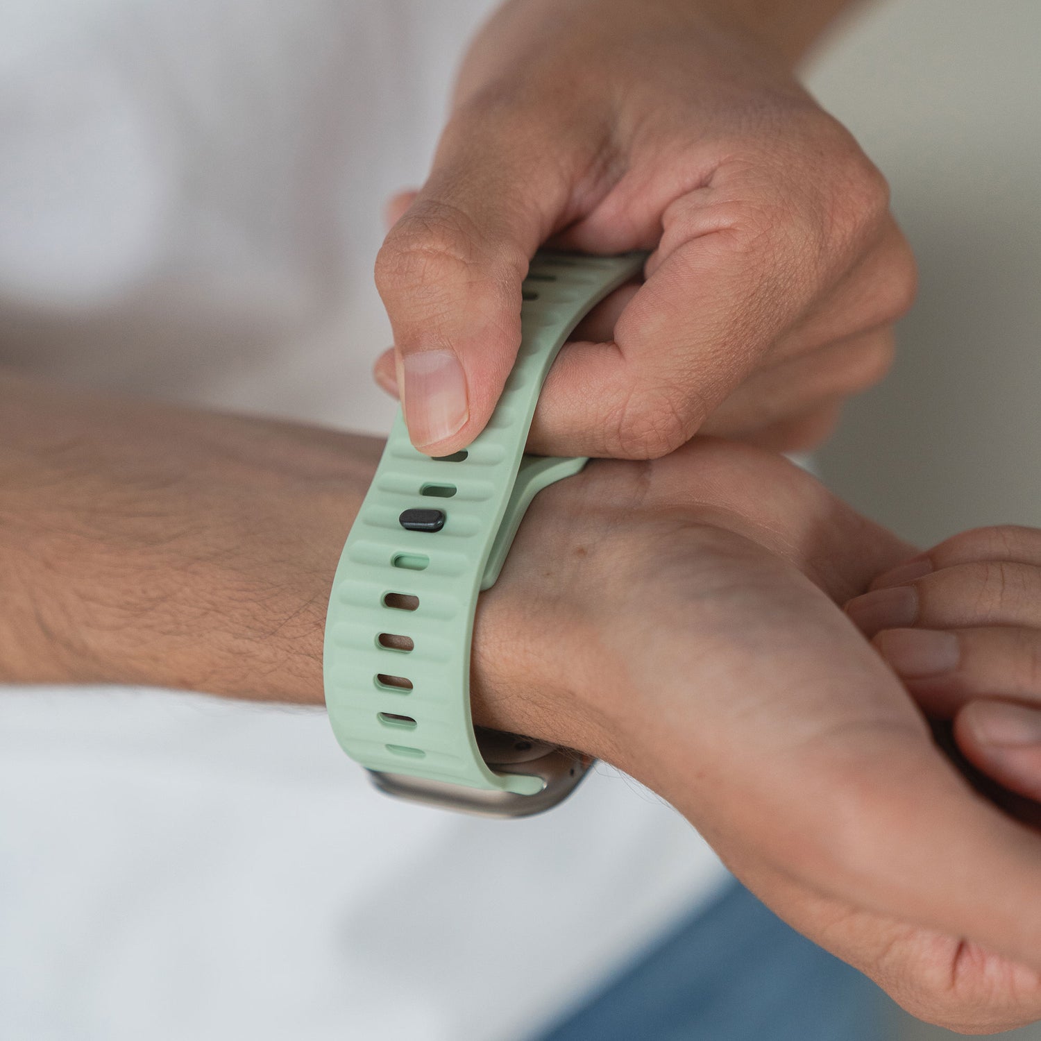 Eine Person befestigt ein arktisband Apple Watch Silikonarmband "Active" in Hellgrün um ihr Handgelenk und verleiht ihrer Apple Watch einen sportlicheren Look. Eine Hand richtet das Armband, während die andere es hält. So kommen beide Hände und das stylische arktisband gut zur Geltung.