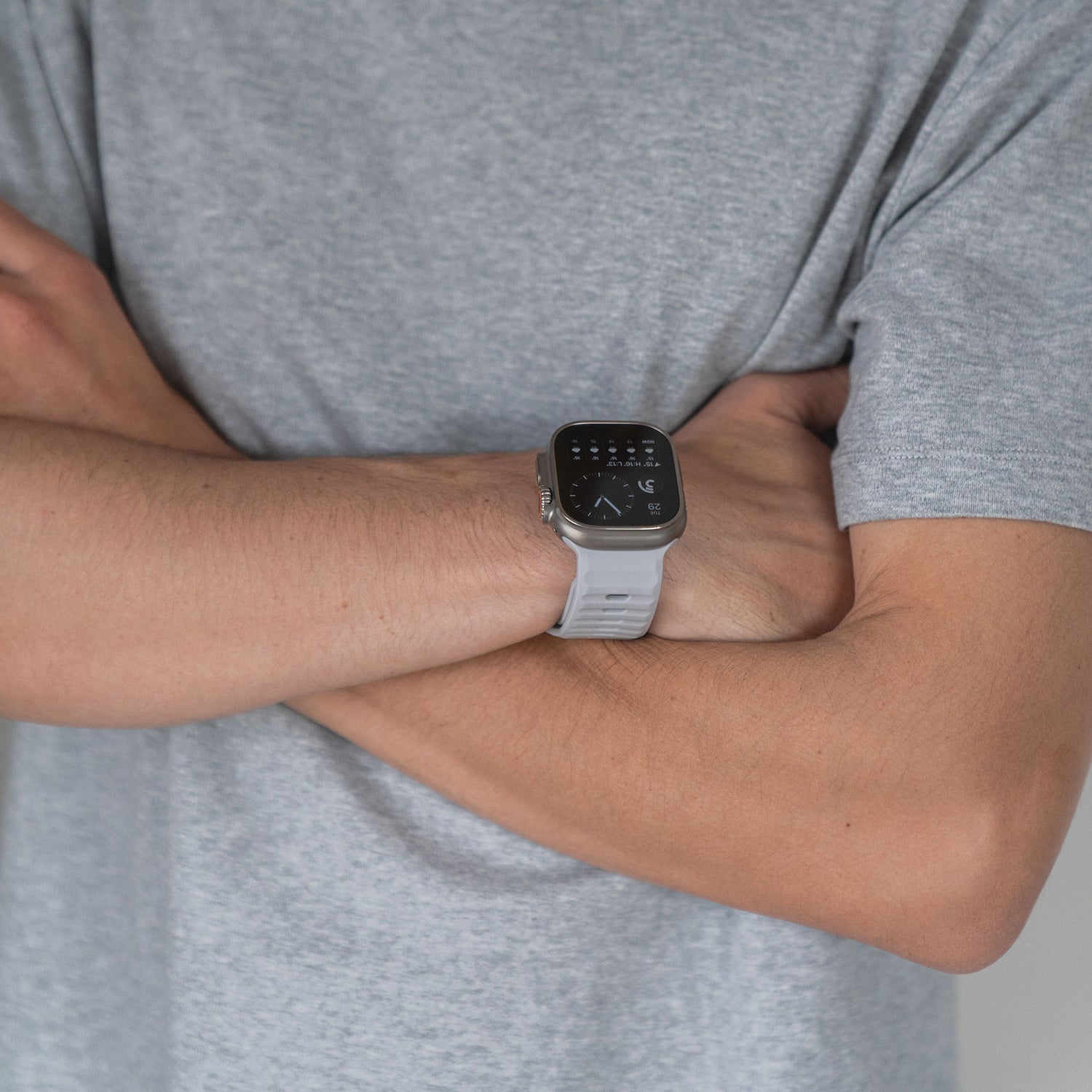 Eine Person im grauen T-Shirt verschränkt die Arme und trägt für einen sportlichen Look ein Arktisband Apple Watch Silikonarmband „Active“ in Weiß am linken Handgelenk.