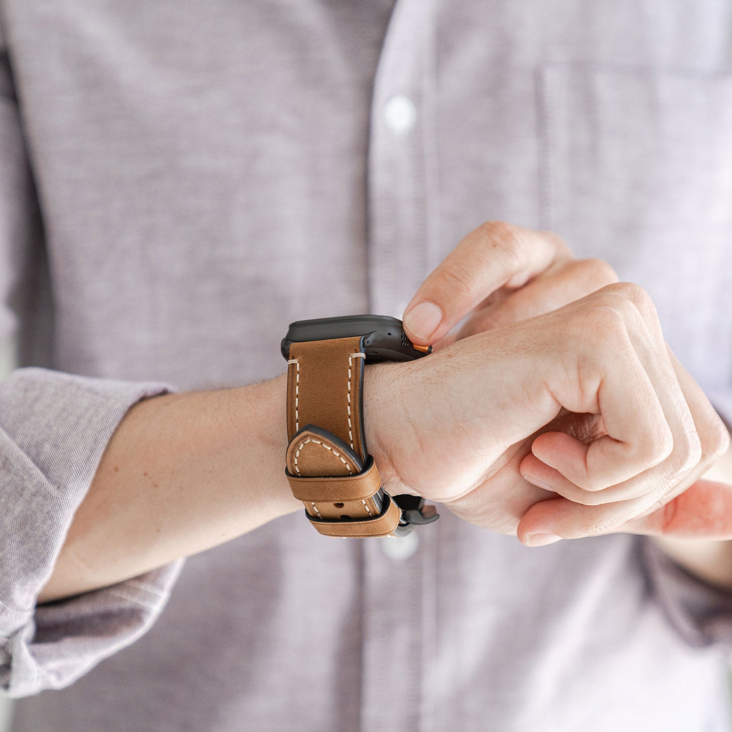 Eine Person in einem hellvioletten Hemd rückt ihre Apple Watch Ultra mit dem arktisband PALERMO GRANDE Lederarmband in Braun (316L Edelstahl) an ihrem Handgelenk zurecht und konzentriert sich dabei auf die Uhr und die Zeiger, während ihr Gesicht nicht zu sehen ist.