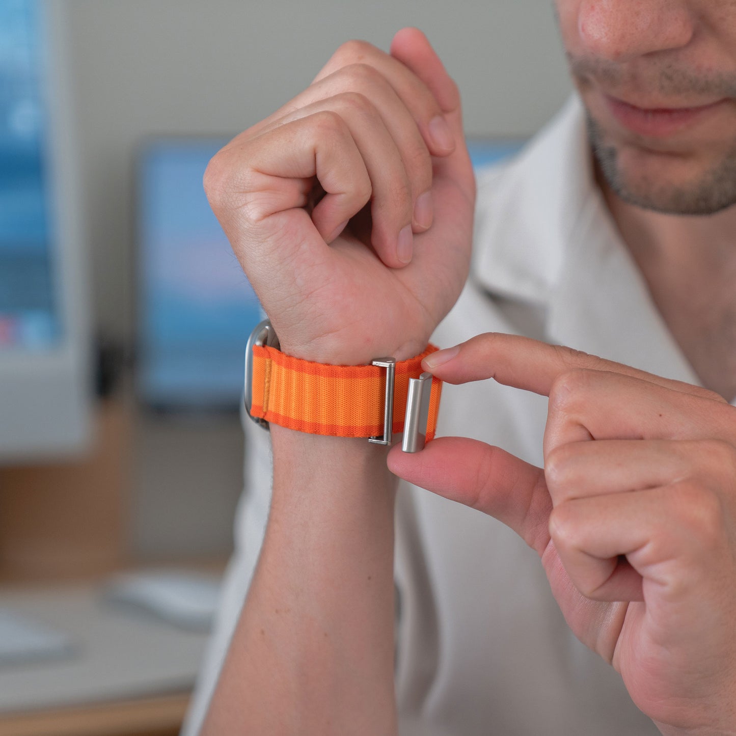 Eine Person befestigt im Innenbereich ein orangefarbenes Arktisband Apple Watch Nylonarmband „Venture“ mit Wellendesign um ihr Handgelenk.