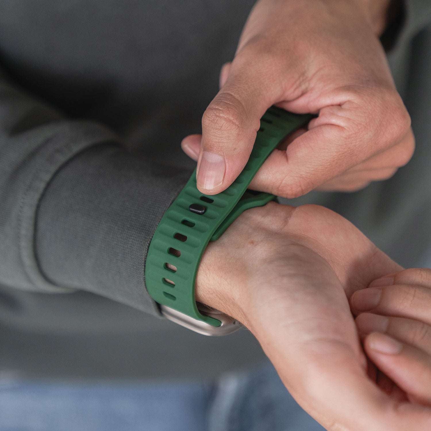 Eine Person befestigt das grüne arktisband Apple Watch Silikonarmband „Active“ von arktisband um ihr Handgelenk und trägt ein dunkles Sweatshirt.