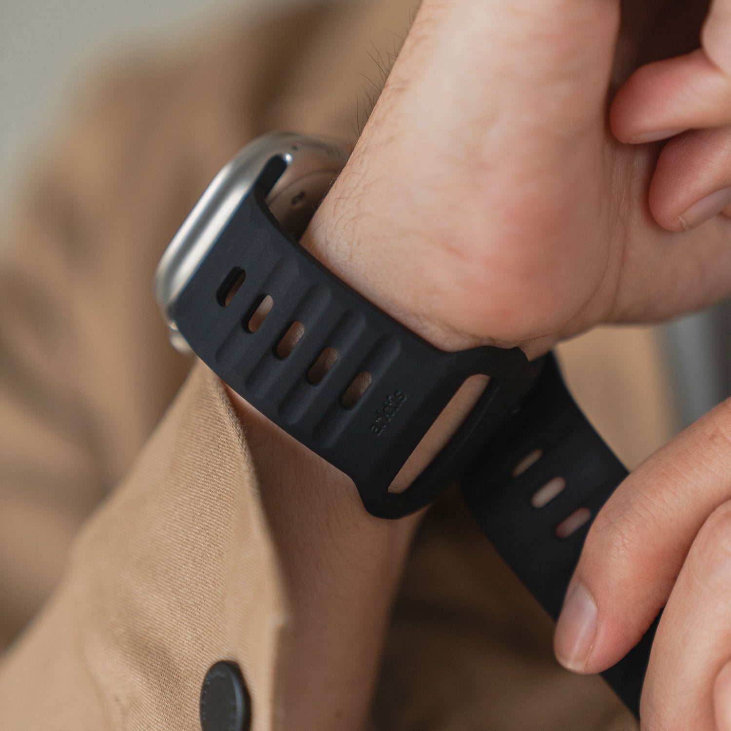 Eine Person in einem hellbraunen Mantel befestigt das arktisband Apple Watch Silikonarmband „Active“ von arktisband mit atmungsaktivem Design an ihrem Handgelenk.