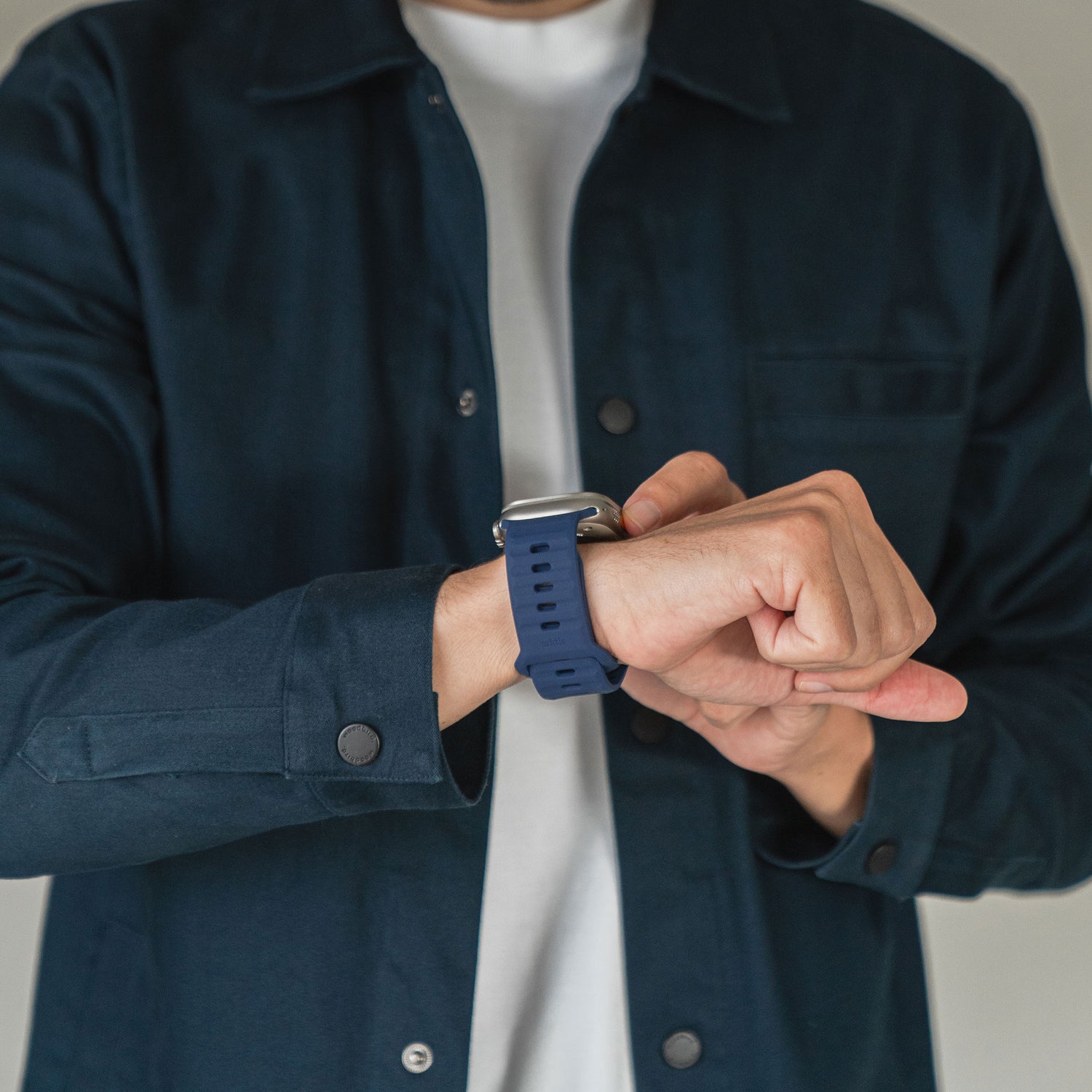 Eine Person in dunkelblauer Jacke und weißem Hemd rückt ein Arktisband Apple Watch Silikonarmband „Active“ an ihrem Handgelenk zurecht, wobei ihr Gesicht nicht zu sehen ist.