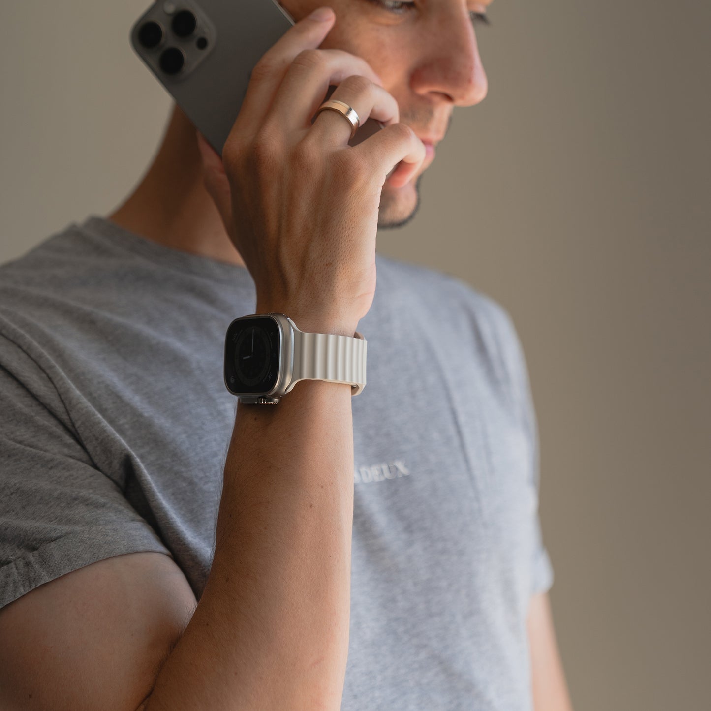 Mann mit grauem T-Shirt und weißem arktisband Apple Watch Sportarmband "Motion" von arktisband, der sich ein Telefon ans Ohr hält und zur Seite schaut.
