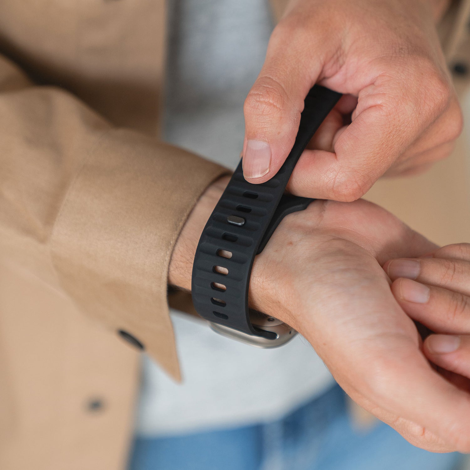 Eine Person in beiger Jacke und grauem Hemd befestigt ein Arktisband Apple Watch Silikonarmband „Active“ in Schwarz mit atmungsaktivem Design an ihrem Handgelenk.