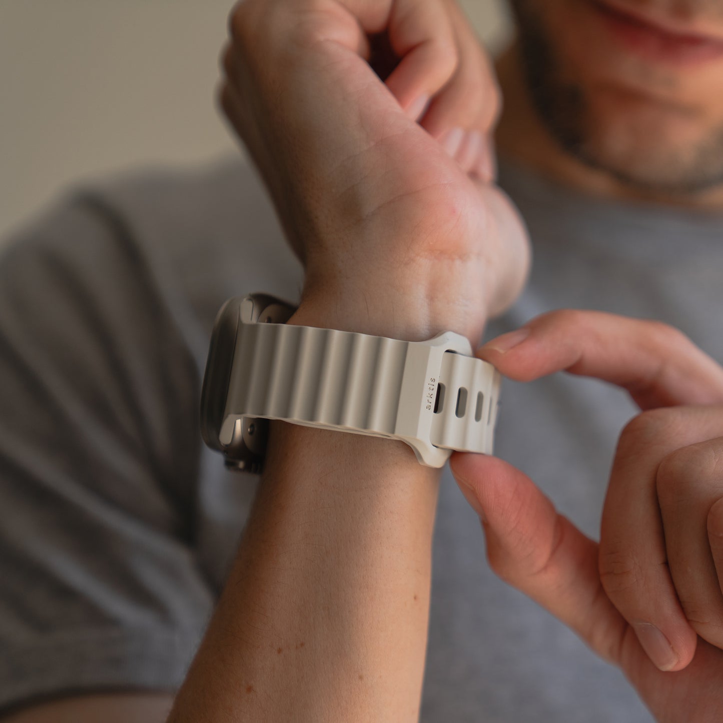 Jemand legt sich das arktisband Apple Watch Sportarmband "Motion" mit einem grauen wellenförmigen Design von arktisband um sein Handgelenk.
