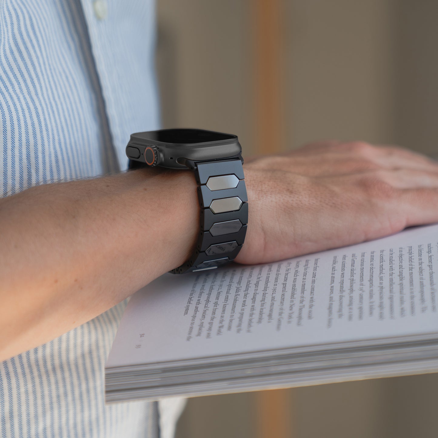 Eine Person trägt ein Arktisband Apple Watch Ultra Titanarmband "Vectoron" und hält mit einer Hand ein offenes Buch.
