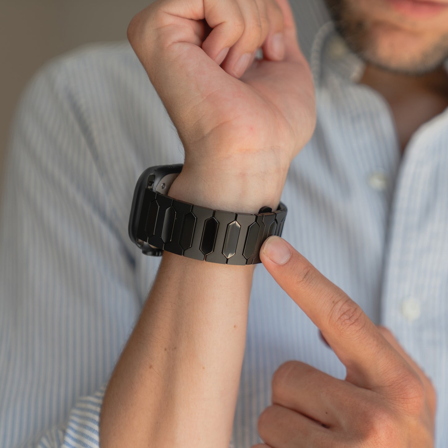 Eine Person in einem hellblau gestreiften Hemd zeigt auf das schwarze Arktisband Apple Watch Ultra Titanarmband "Vectoron" mit DLC-Beschichtung an ihrem Handgelenk.