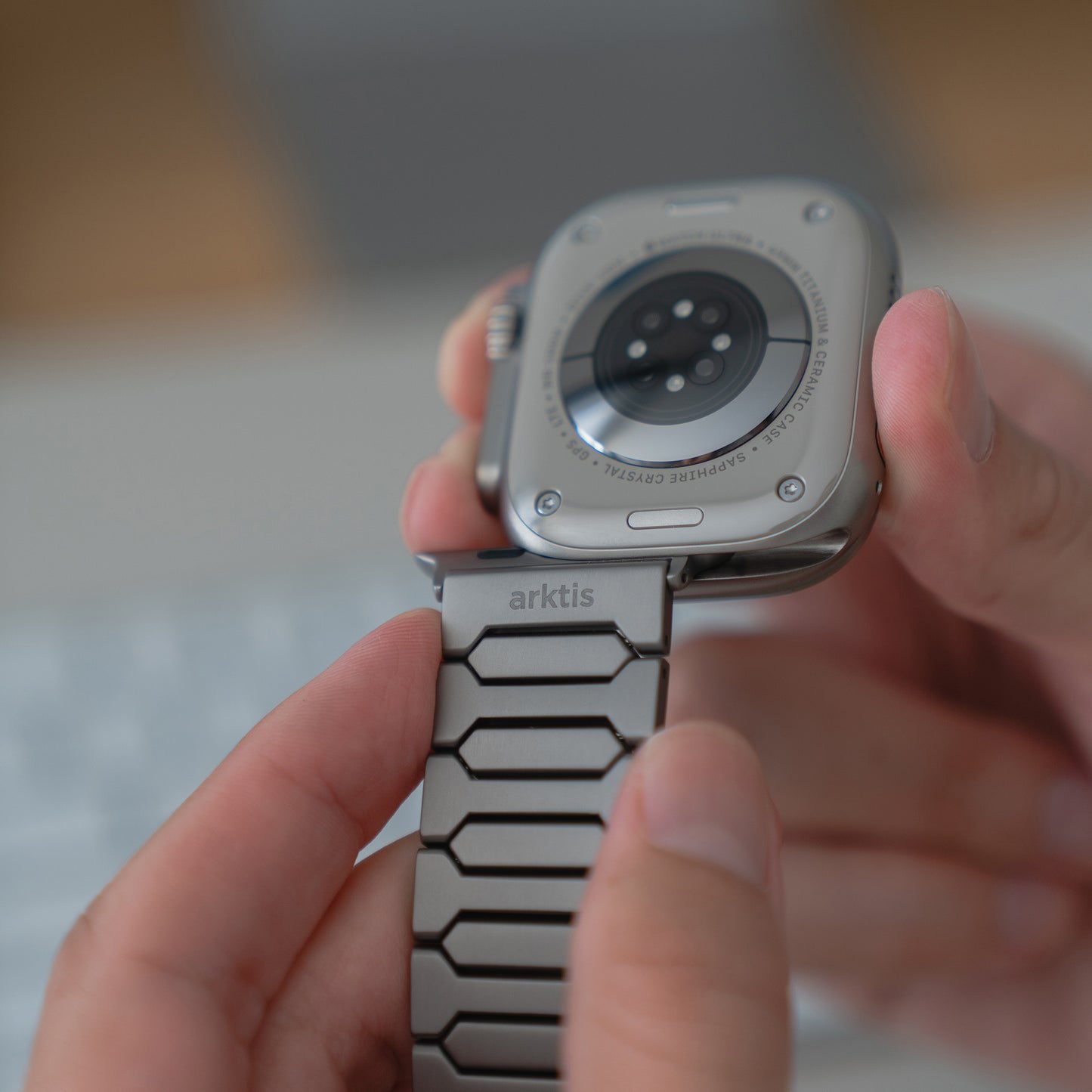 Eine Person hält das Arktisband Apple Watch Ultra Titanarmband "Vectoron" und konzentriert sich dabei auf die Rückseite der Uhr und die Titanschließe.