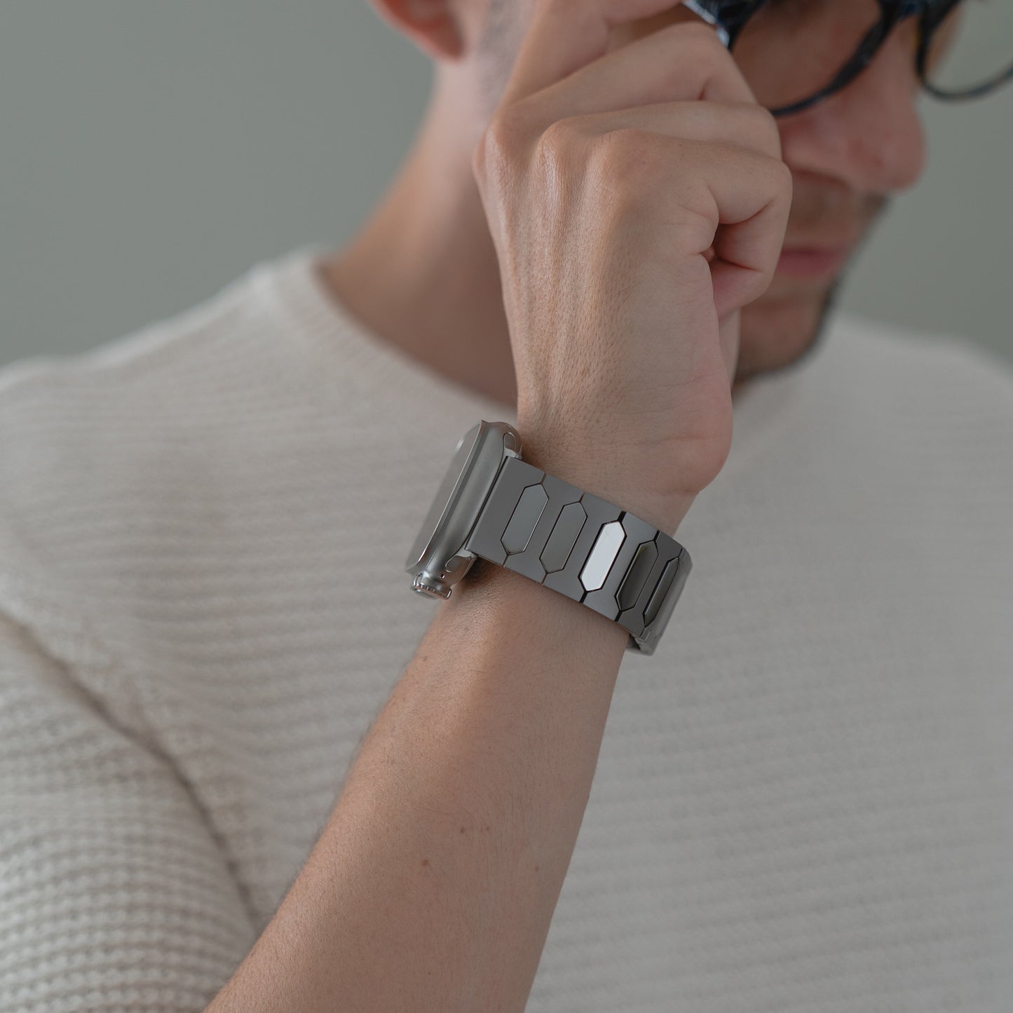 Eine Person in einem weißen Pullover rückt eine Brille zurecht, während sie das arktisband Apple Watch Ultra Titanarmband "Vectoron" von arktisband am Handgelenk trägt.