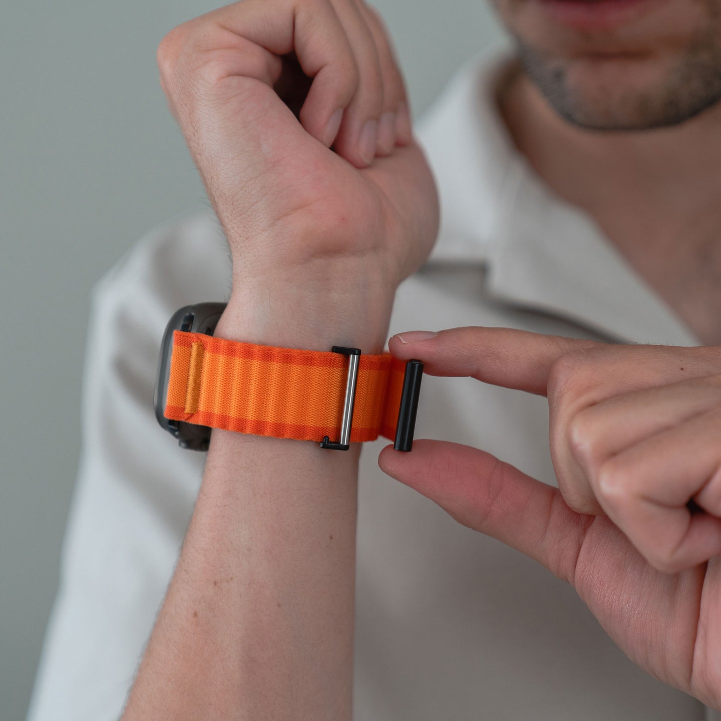 Eine Person passt den Verschluss des arktisband Apple Watch Nylon Armband „Venture“ in Orange an ihrem Handgelenk an – ideal für Outdoor-Fans, die einen stylischen Wellen-Look lieben.